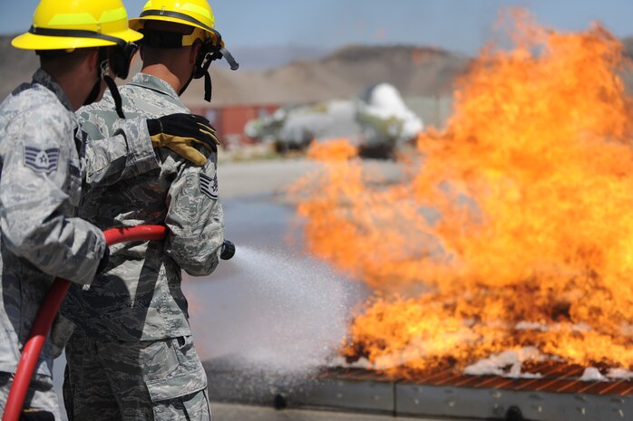 Two  members of the 99th Ground Combat Training Squadron extinguish a fire during the inaugural fire fighting training course held at Creech Air Force Base Aug. 7. The Creech fire department trained members of the 99th GCTS on basic fire fighting skills to help contain fires at the security forces training site, Silver Flag Alpha. (U.S. Air Force photo by Senior Airman Brian Ybarbo)