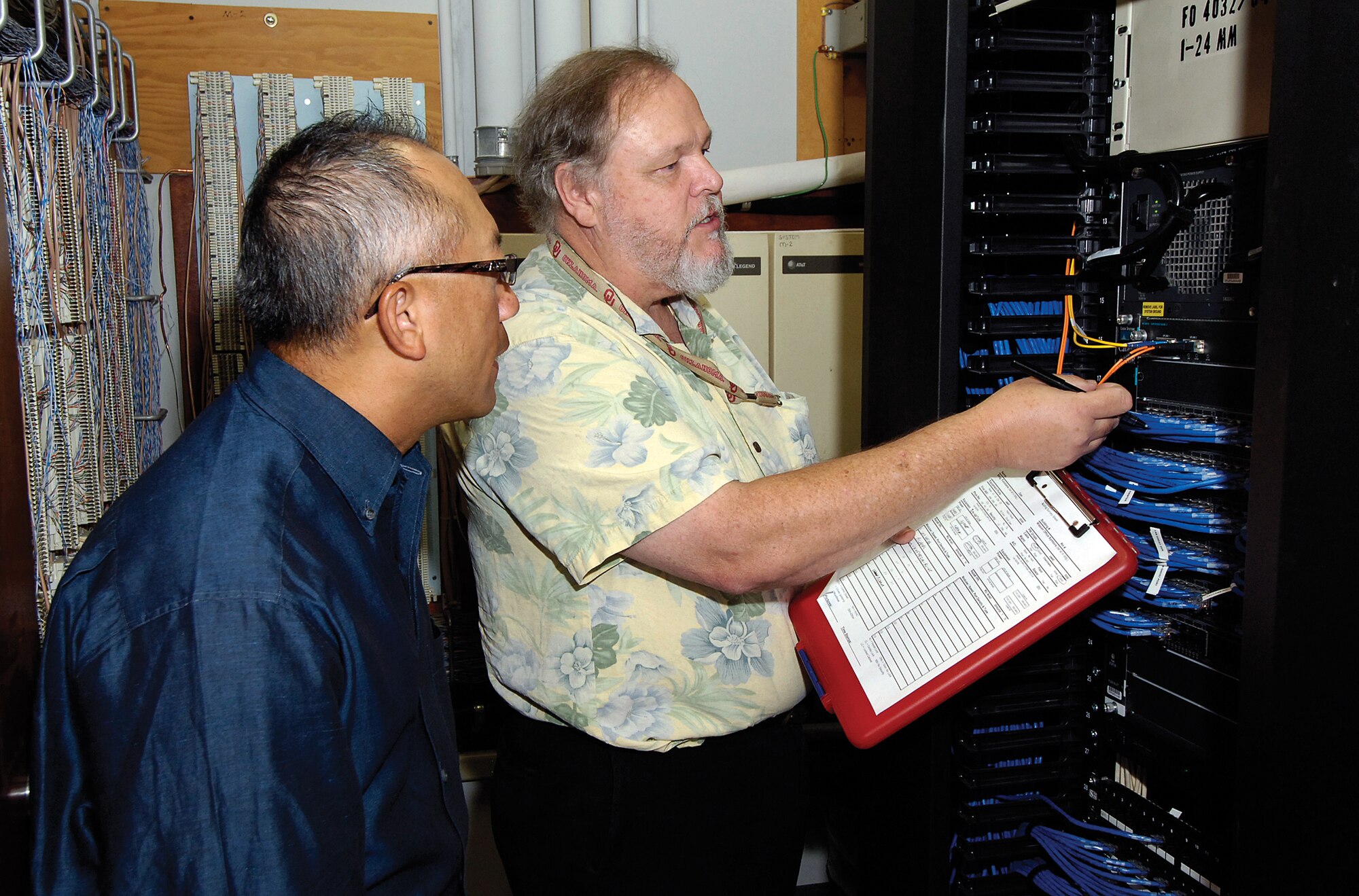 Fred Peake, right, a 38th Cyberspace Engineering Group systems telecommunications manager, reviews with Thanh Alcorn, a Network Branch lead engineer in the 38th Engineering and Implementation Division, how to verify devices on the network. Six teams of two recently began this task which will take them to more than 300 such communications closets across base. (Air Force photo by Margo Wright)
