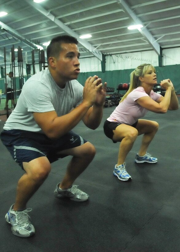 JOINT BASE ANDREWS, Md. -- Jill Ritenauer, 316th Force Support Squadron secretary, instructs Senior Airman Eric Barrera, 316 FSS career development representative, on the proper form of a squat exercise during a bi-weekly CrossFit workout session she monitors in the Tactical Fitness room, at the West Fitness Center Aug. 4. Ritenuaer is a Level One CrossFit coach and is the squadron’s unit fitness program monitor. (U.S. Air Force photo by Bobby Jones) 