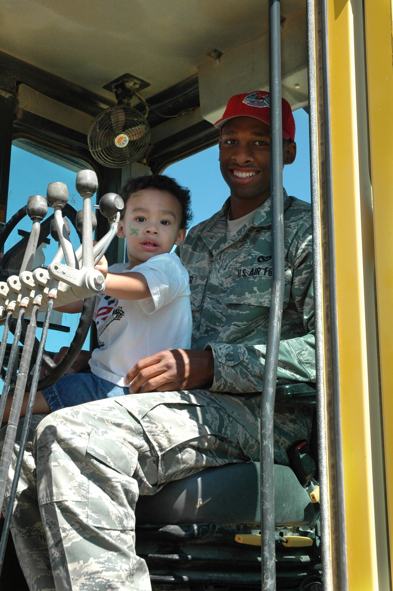 Airman 1st Class Brandon Fisher, 819th RED HORSE Squadron heavy equipment operator, and his son, Brandon Jr., pause for a photo during a youth deployment line July 30, 2010, outside the Youth Programs Center at Malmstrom Air Force Base, Mont. Children who came to the event got to experience what their parents experience when processing through a deployment line, but with a fun twist that included games, barbecued hot dogs, and a chance to climb into the cab of some RED HORSE heavy equipment, which the squadron deploys with to build and repair flightlines and base infastructure. (U.S. Air Force photo/Senior Airman White)