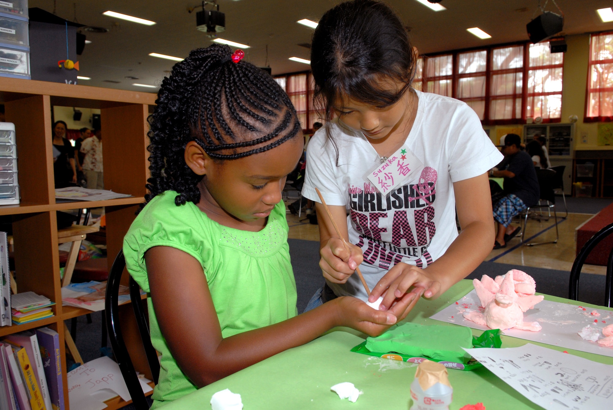 Mykia Moses (left) gets a helping hand making a Shisa dog from Suzuka Teruya (right) Aug. 5, 2010, at Kadena Air Base, Japan. The two children took part with about 40 others in an international exchange program organized by the Kadena Youth Center and the Chatan Town Lions Club here. In addition to making Shisa dogs, the children played ping pong, pool, and other games, and ate lunch at the base exchange food court here. (U.S. Air Force photo/Junko Kinjo)