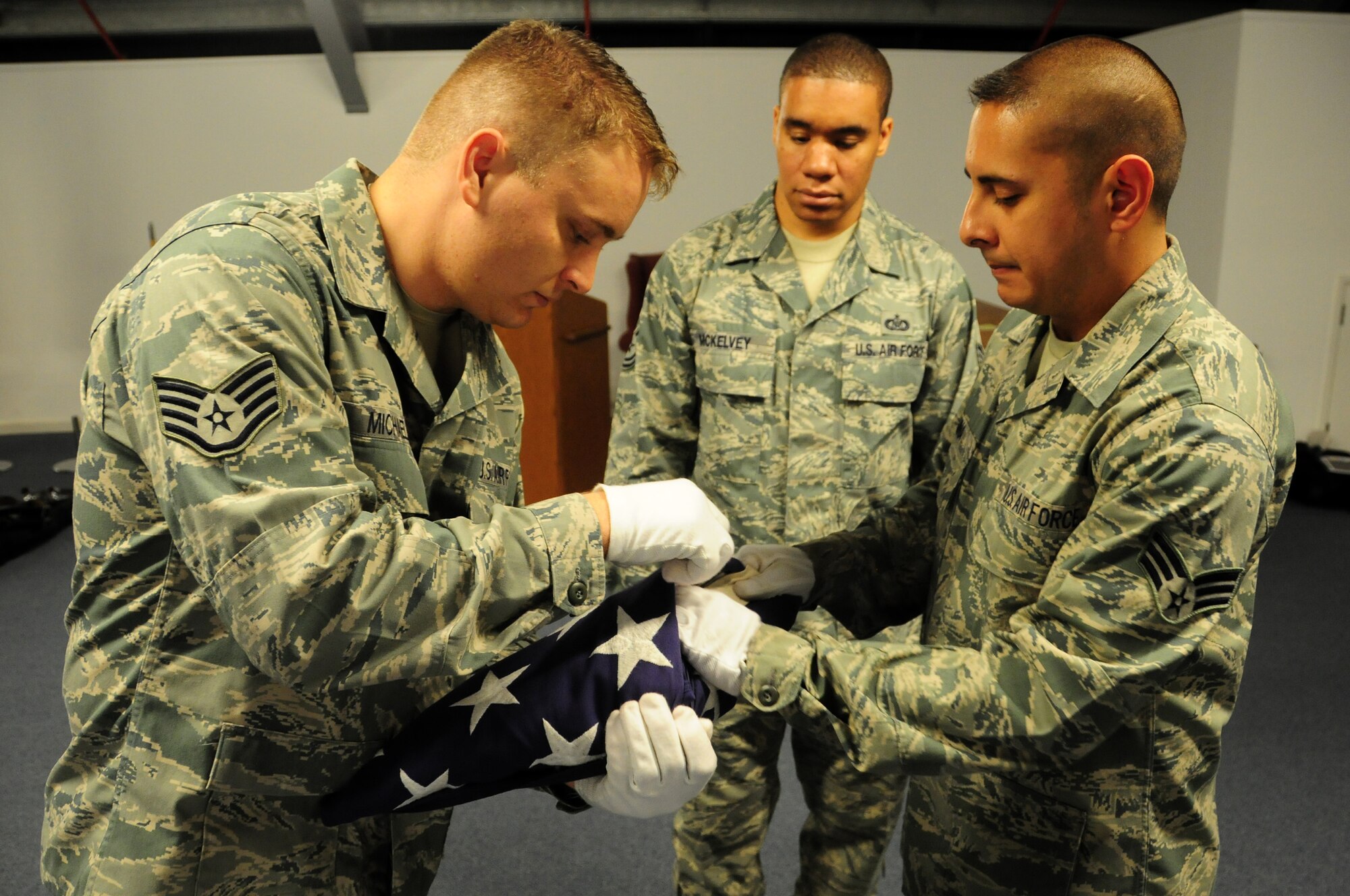 Tech Sgt. Cory McKelvey, 48th Fighter Wing Command Post NCO in-charge or reports (middle), observes Staff Sgt. Allen Michaels, 48th Component Maintenance Squadron avionics technician (left), and Senior Airman Michael Luna, 748 Aircraft Maintenance Squadron programs manager, while they perform a two-person flag fold. Sergeant McKelvey has been on the honor guard for six years and is one of the trainers at Lakenheath. (U.S. Air Force photo/Airman 1st Class Lausanne Morgan)