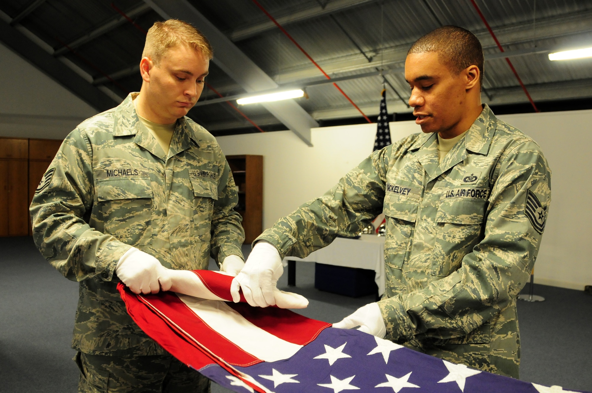 Tech Sgt. Cory McKelvey, 48th Fighter Wing Command Post NCO in-charge or reports (right), aids Staff Sgt. Allen Michaels, 48th Component Maintenance Squadron avionics technician, in properly folding a flag Aug. 4 at RAF Lakenheath. Sergeant Michaels was practicing for his honor guard certification. (U.S. Air Force photo/Airman 1st Class Lausanne Morgan)