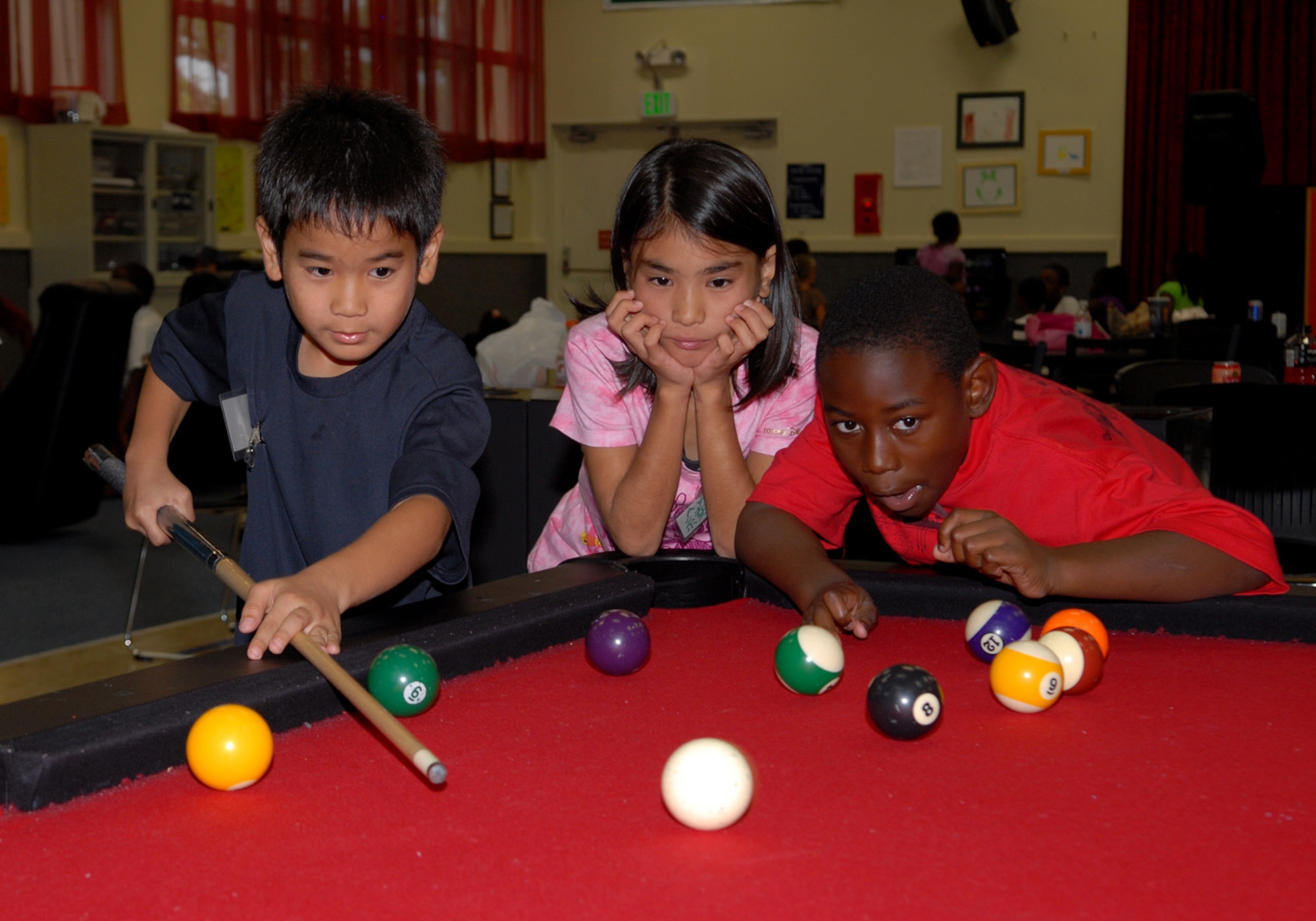 Yuuri Kijyoka (left) prepares to shoot a pool ball while Ayaka Chibana (center), 10, from Yomitan Elementary school and Carlton Furman (right), 9, from Zion Christian School, watch (U.S. Air Force Photo/Junko Kinjo)