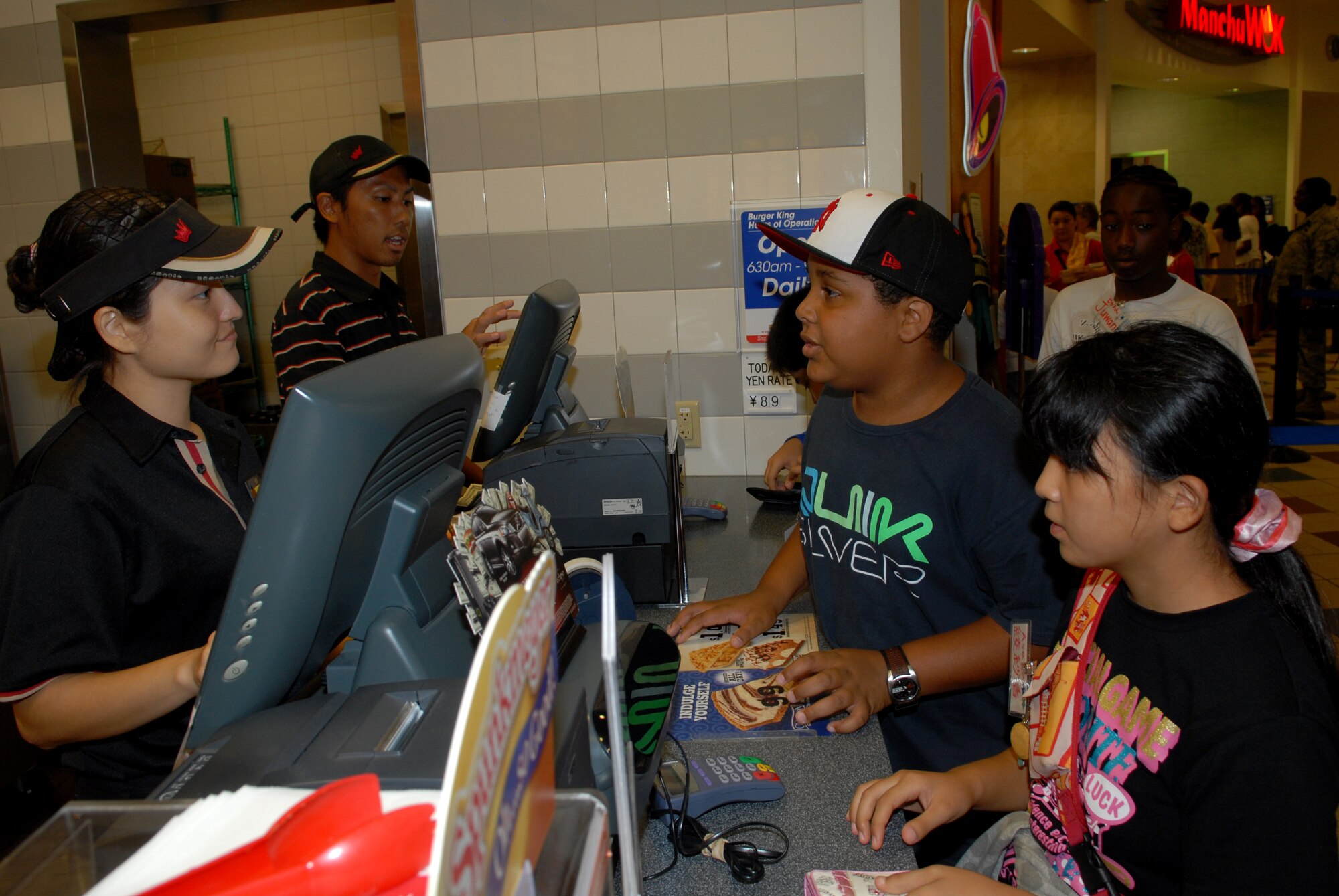 Asaka Tamaki (right) orders lunch by using English and paying in American dollars with help from partner Ethan Stewart (left) at the Kadena food court Aug. 5. The international exchange was done between the children from Chatan Town Lions Club and Kadena Youth center through making Shi-Shi dogs, ping pong, pool, TV games, arm wrestling and more. (U.S. Air Force Photo/Junko Kinjo)