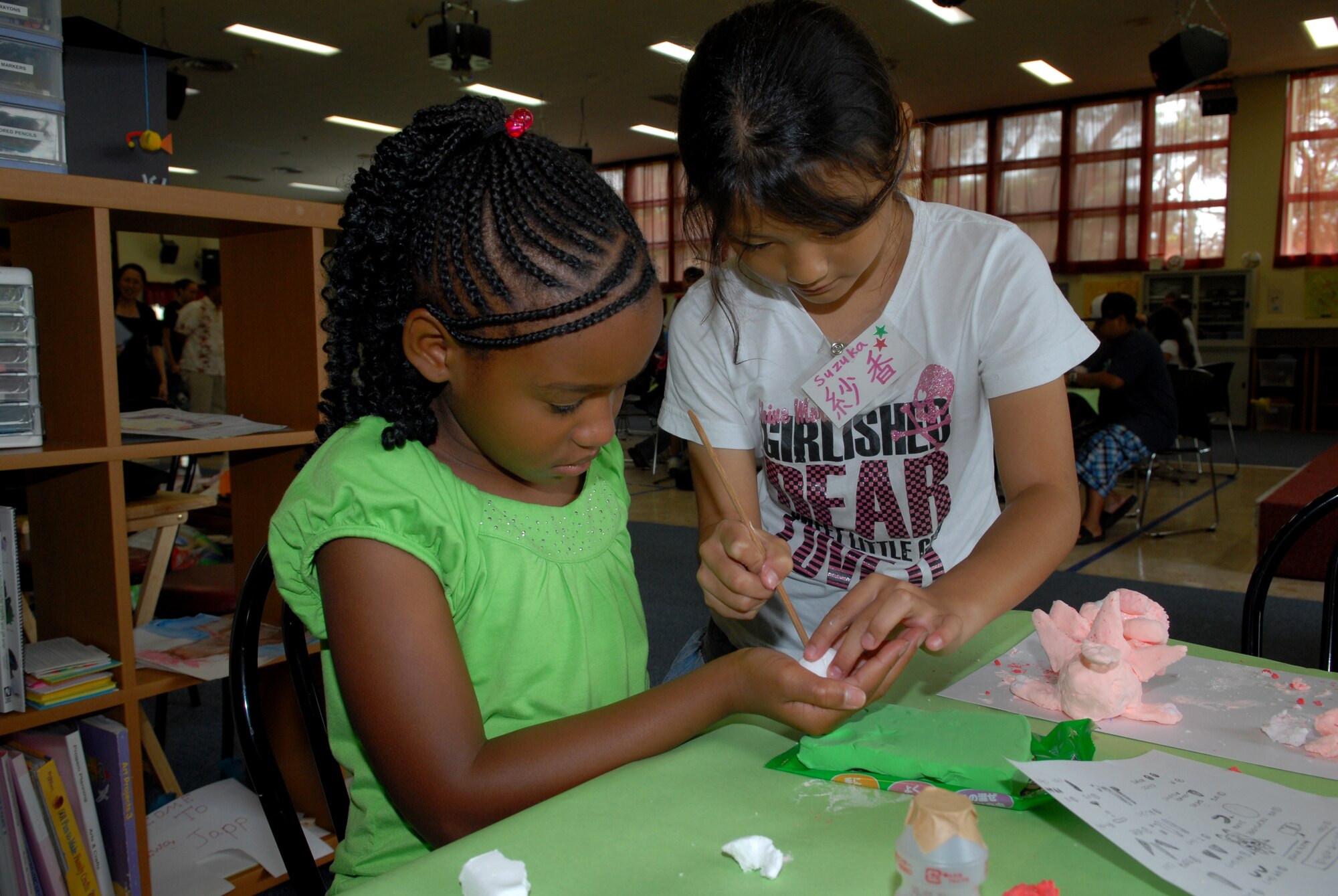 Mykia Moses (left), 9, from Amelia Earhart Intermediate School  gets a helping hand making Shi-Shi dog  from Suzuka Teruya (right), 9, from Hamagawa Elementary school. The international exchange was done between the children from Chatan Town Lions Club and Kadena Youth center through making Shi Shi dogs, ping pong, pool, TV games, arm wrestling and more. (U.S. Air Force Photo/Junko Kinjo)