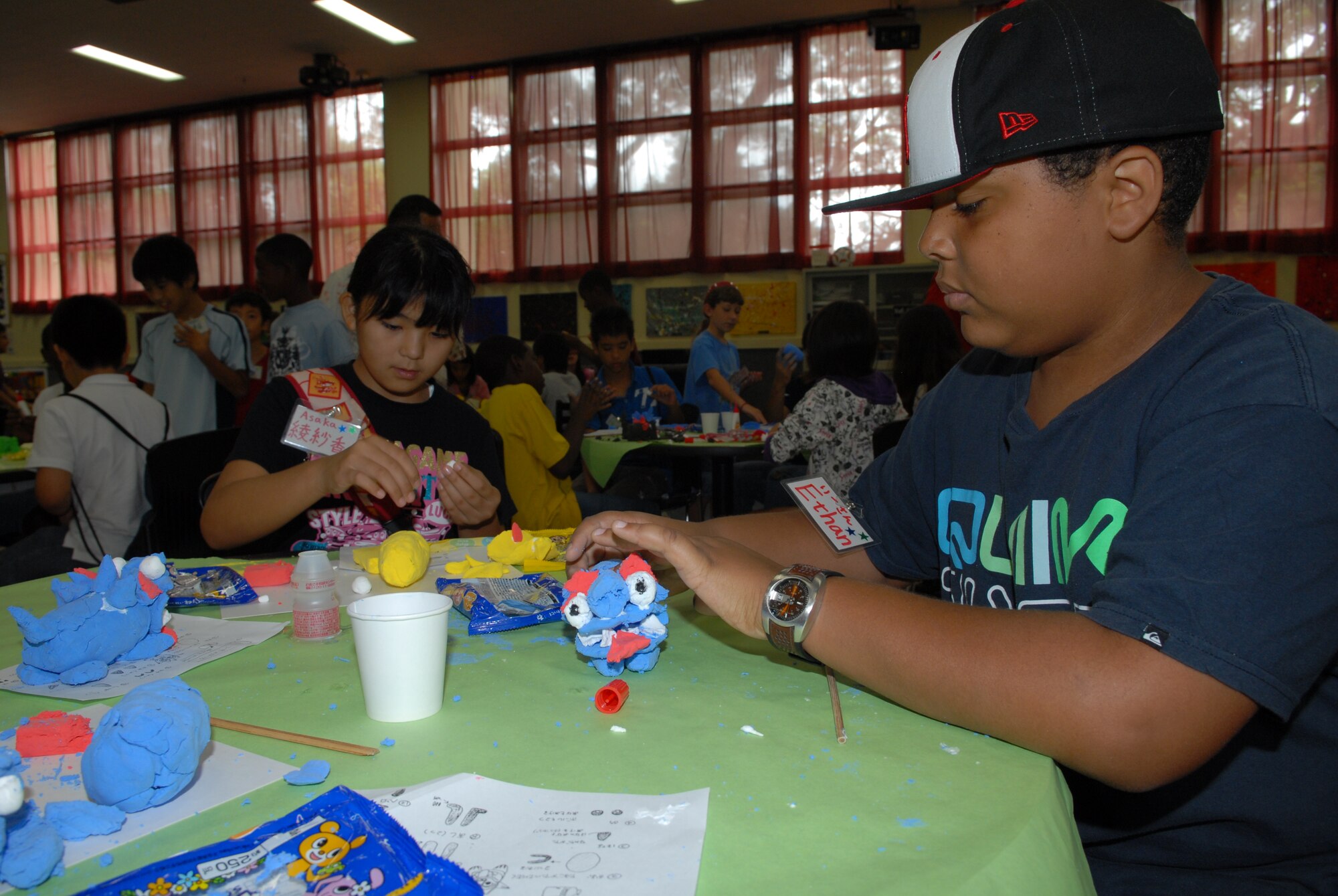 Asaka Tamaki (left), 11, from Hamagawa Elementary school with partner  Ethan Stewart (right), 11, from Kadena Middle School work on their Shi-Shi dogs together at the Kadena Youth center Aug. 5. The international exchange was done between the children from Chatan Town Lions Club and Kadena Youth center through making Shi-Shi dogs, ping pong, pool, video games, arm wrestling and more. (U.S. Air Force Photo/Junko Kinjo)