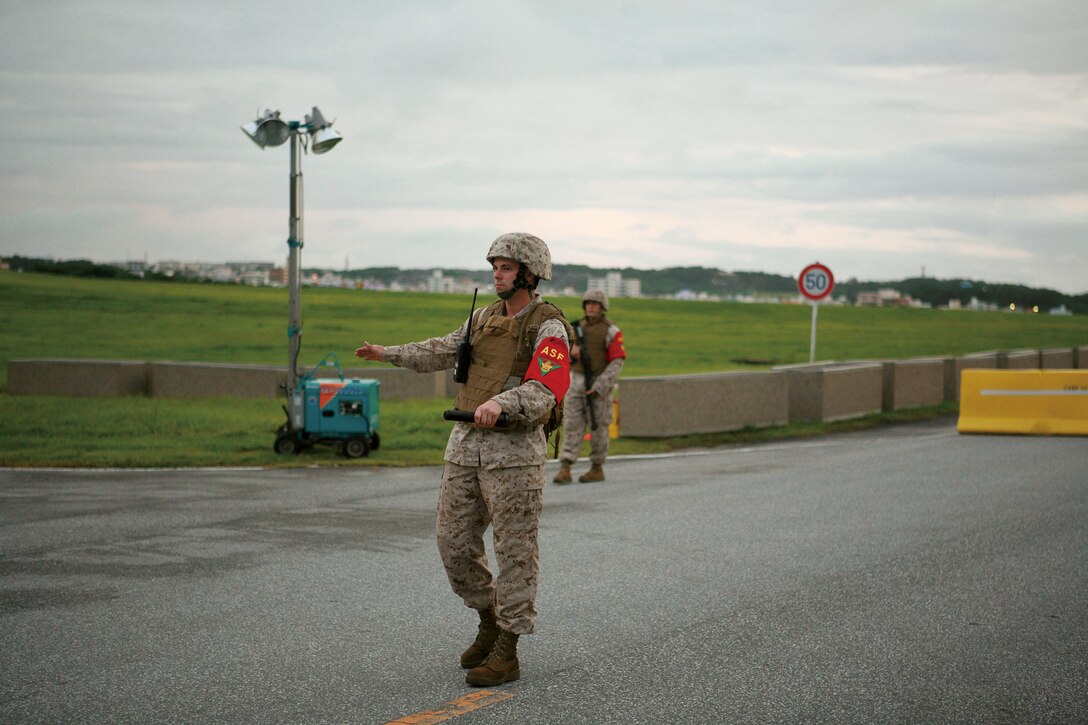 Lance Cpl. Kevin Harper, left, a CH-46E Sea Knight avionics mechanic with Marine Medium Helicopter Squadron 265, Marine Aircraft Group 36, 1st Marine Aircraft Wing, III Marine Expeditionary Force, and Lance Cpl. Joshua J. Vega, right, a flight equipment worker with Marine Aviation Logistics Squadron 36, MAG-36, both Auxiliary Security Forces Marines, direct traffic while guarding the road leading to the Futenma Flightline Fair on Marine Corps Air Station Futenma Aug. 8.