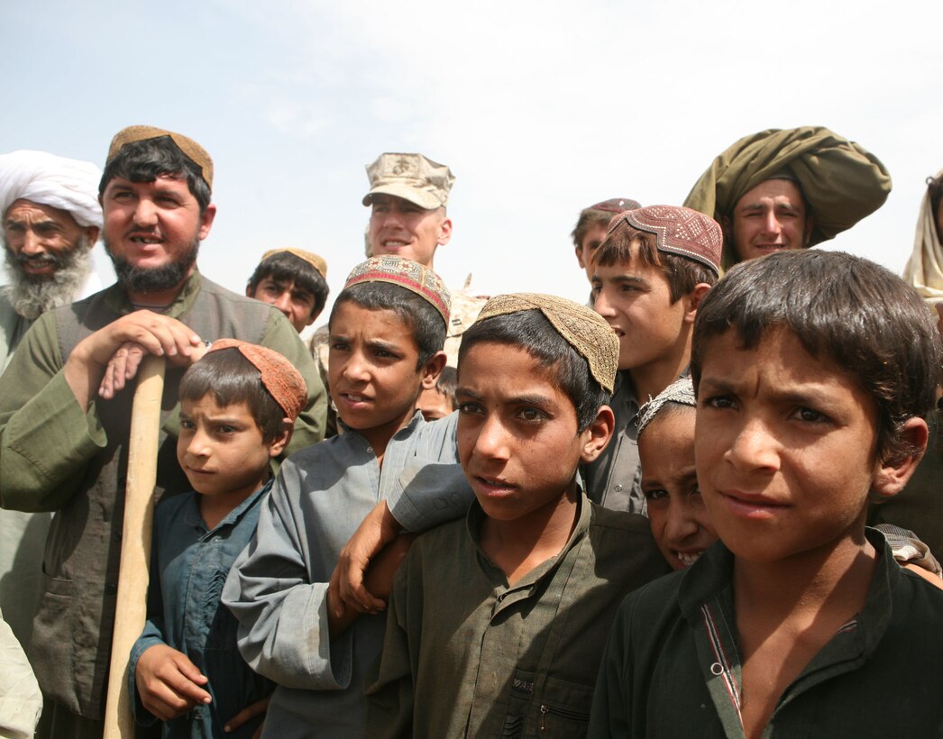 Afghan children listen as the Marjah district education director, Nazar Khan Taukalyar, reveals plans for a new school in the Koreh Chareh bazaar area during a school ground-breaking ceremony in Marjah, Afghanistan, Aug. 9, 2010.