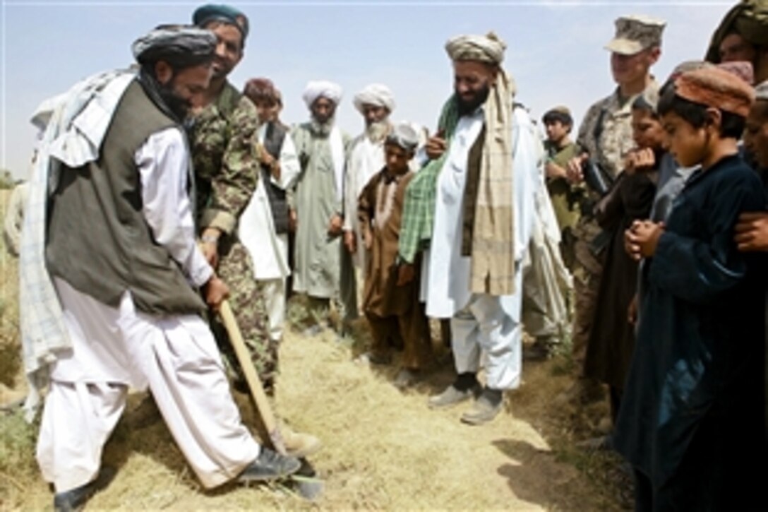 Yar Mohammad Barak, Marja district governor, plants a shovel into the ground near the Koreh Chareh bazaar to break ground for a new primary school as a U.S. Marine looks on in Marja, Afghanistan, Aug. 9, 2010. The Marine is assigned to the 2nd Battalion, 6th Marine Regiment.