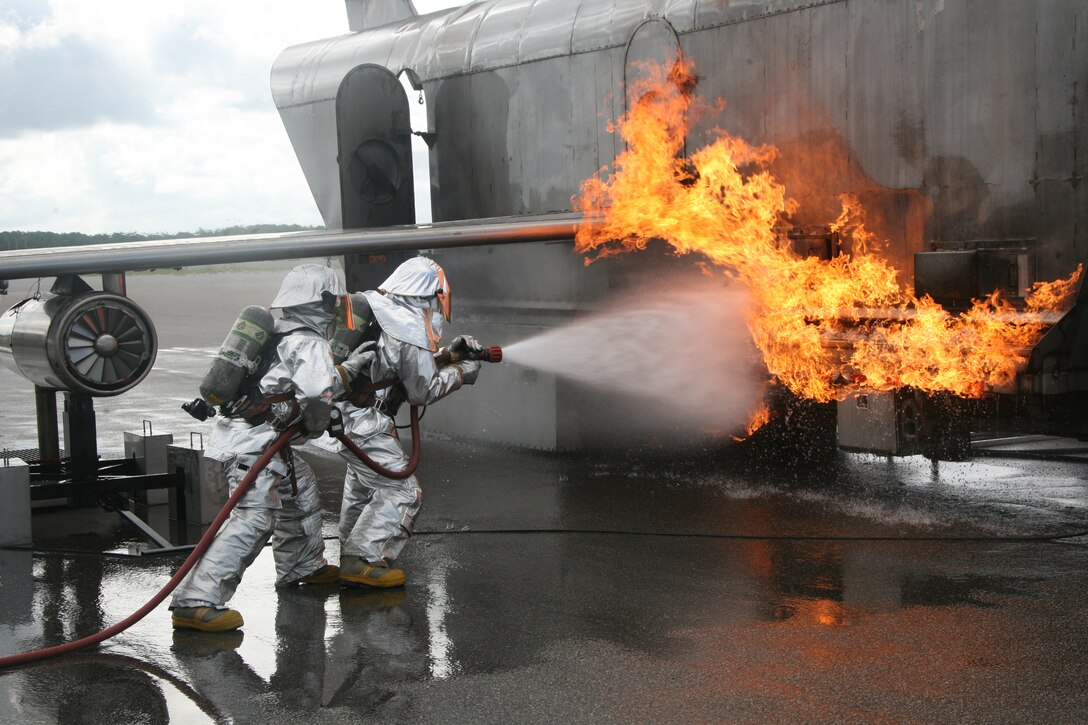 Sgt. Maj. Thomas E. Sherwood and an aircraft rescue firefighter attack the exterior fire that has erupted outside of the mobile aircraft fire training device during a training exercise Aug. 10. ::r::::n::“This training gives me a deeper respect for the ARFF Marines and what they do for the air station,” said Sherwood, the squadron sergeant major for Headquarters and Headquarters Squadron, Marine Corps Air Station Cherry Point.::r::::n::
