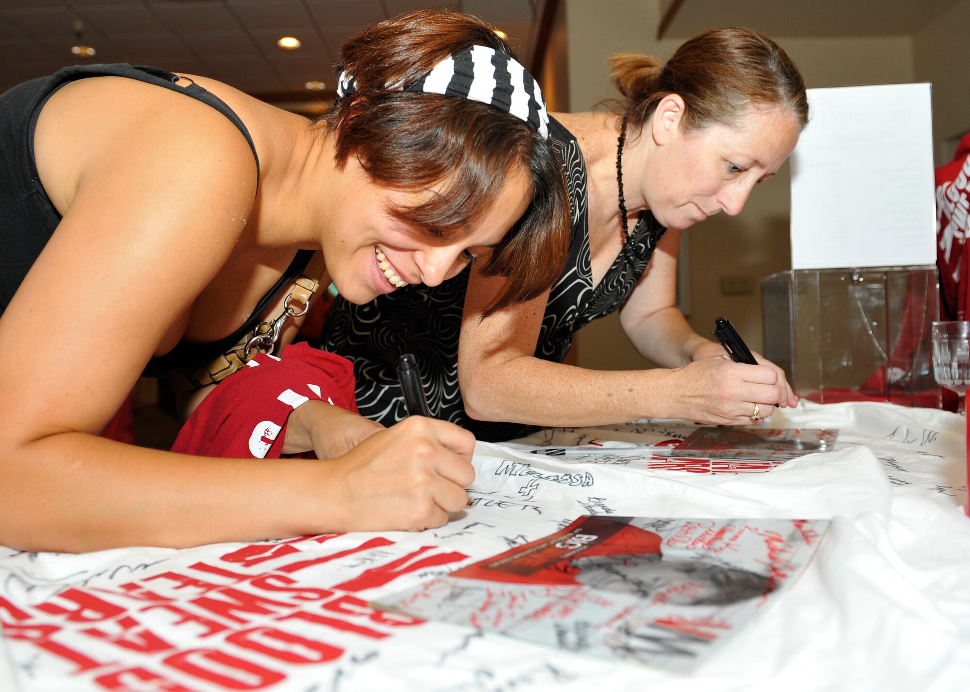HOLLOMAN AIR FORCE BASE, N.M.  -- Brenda Wheeler, wife of Master Sgt. Thomas Wheeler, 49th Maintenance Squadron and Vanessa Welch, wife of Staff Sgt. Jason Welch, 49th Aircraft Maintenance Squadron, both members of the Big Give team, HUG, sign their names on t-shirts to be given to the team sponsors during the Big Give After Party, Aug. 6, 2010. All nine teams that participated in the Big Give gathered at the Desert Sands Enlisted Club for the After Party, and guest were asked to vote on their favorite teams to win cash prizes. (U.S. Air Force photo by Senior Airman Veronica Stamps / Released)