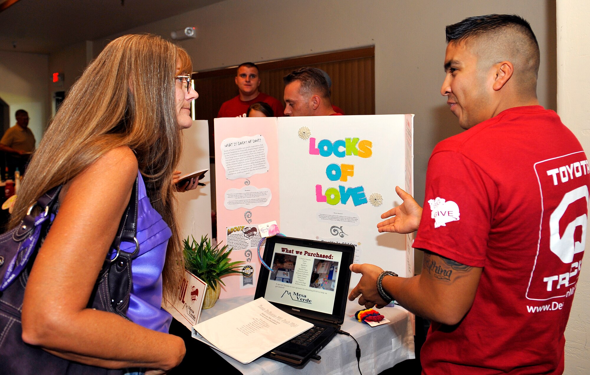 HOLLOMAN AIR FORCE BASE, N.M.  -- Staff Sgt. Kevin Garces, 49th Logistics Readiness Squadron, tells Sally Roberts, 49th Contracting Squadron, about Team POL's mission during the Big Give After Party at the Desert Sands Enlisted Club Aug. 6, 2010. The POL team collected hair donations for the Locks of Love organization. All nine teams who participated in this year's Big Give Project set up booths to display how they gave big for the community. (U.S. Air Force photo by Senior Airman Veronica Stamps / Released)