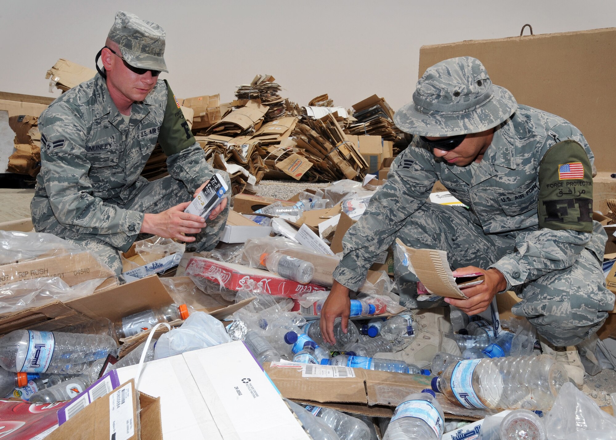 SOUTHWEST ASIA - Airman 1st Class Gregory Nunley and Senior Airman Catalino Vega, 386th Expeditionary Civil Engineer Squadron Force Protection escorts, sort through recyclable materials here July 22, 2010, to ensure that no one has thrown out sensitive items that may pose a risk to base security. Airmen Nunley and Vega are two of approximately 100 Force Protection escorts assigned to the 386th ECES/FP. (U.S. Air Force photo by Senior Airman Laura Turner)