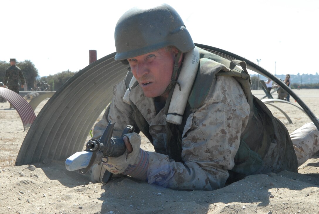 David Sparks, criminal justice teacher, Klein Collins High School, Houston, Texas, shuffles through the sand as he low crawls through the Bayonet Assault Course, wearing Marine desert camouflage, a flak jacket, helmet and gloves, and carrying a rubber M16-A2 service rifle with a plastic bayonet attached on the end.