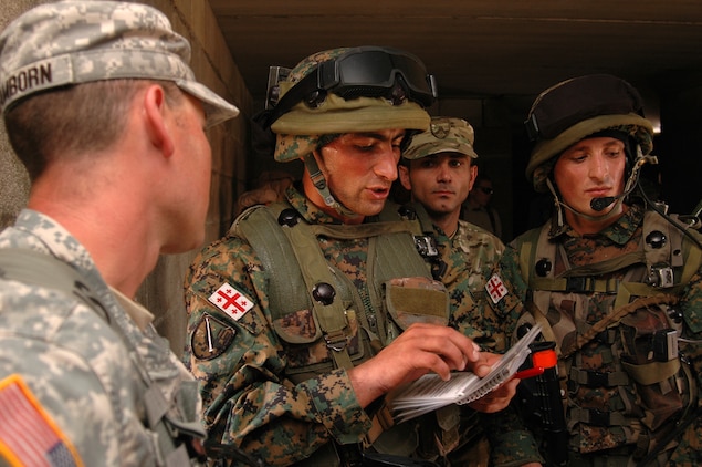 Republic of Georgia Army 2nd Lt. Besik Kapanadze {CENTER}, 3rd Platoon leader, "B" Company, 32nd Light Infantry Battalion, discusses the situational training exercise (STX) with an observer/controller with the Joint Multinational Readiness Center. The Republic of Georgia's 32nd Light Infantry Battalion was conducting cordon searches during their STX training. The STX is the first part of the mission rehearsal exercise, a final evaluation of the 32nd Battalion as they prepare for their deployment to Afghanistan in support of International Security Assistance Forces there.