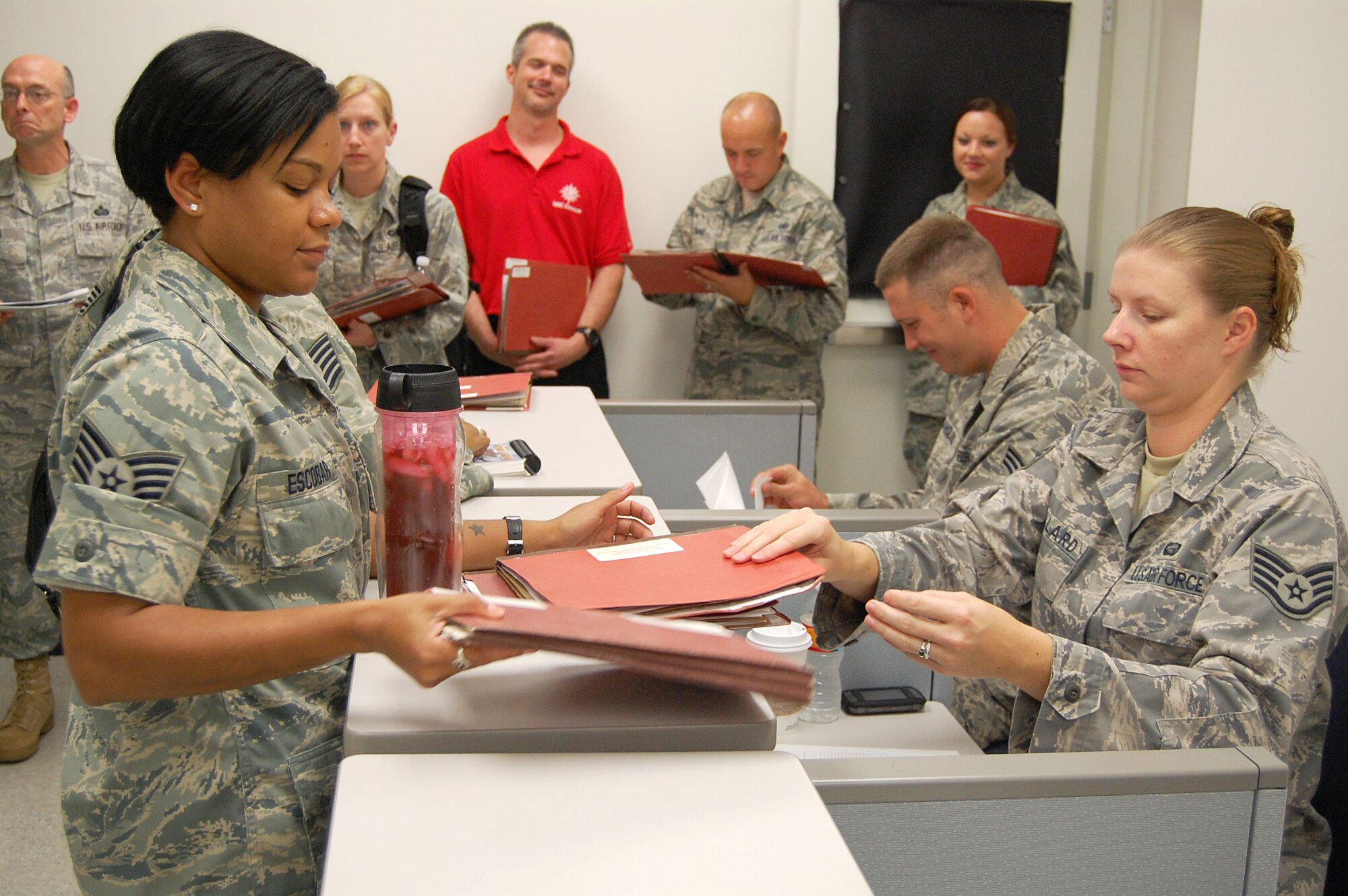 Staff Sgt. Jessica Escobar, Air Force Personnel Center Unit Deployment manager, left, hands Staff Sgt. Stacceye Stallard, 902nd Force Support Squadron, mobility deployment folders at the 902nd Logistics Readiness Squadron Deployment Processing Center on Randolph Air Force Base Aug. 10 during exercise Joint Base San Antonio 10-08. More than 200 Airmen from different agencies on Randolph AFB participated in the two-day deployment exercise. (U.S. Air Force photo/Master Sgt. Paul Kilgallon)