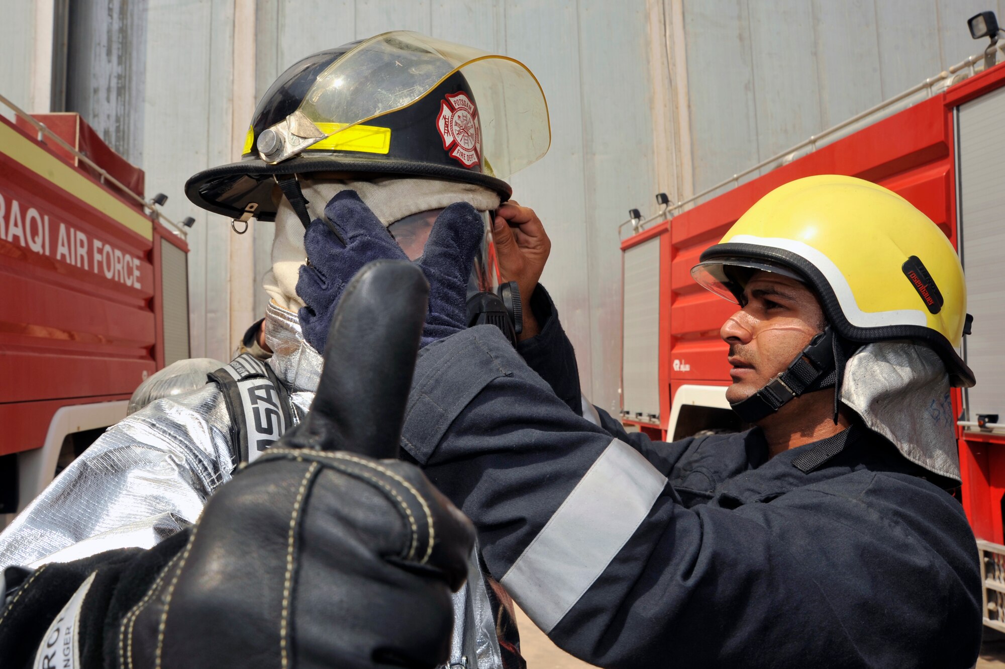 An Iraqi air force firefighter gives the thumbs up while another firefighter ensures he is completely covered up for protection, Aug. 5, 2010, at New Al Muthana Air Base, Iraq. Firefighters must ensure their Nomex hood covers all exposed skin on their head to prevent burns.( U.S. Air Force photo by Senior Airman Perry Aston) (Released)