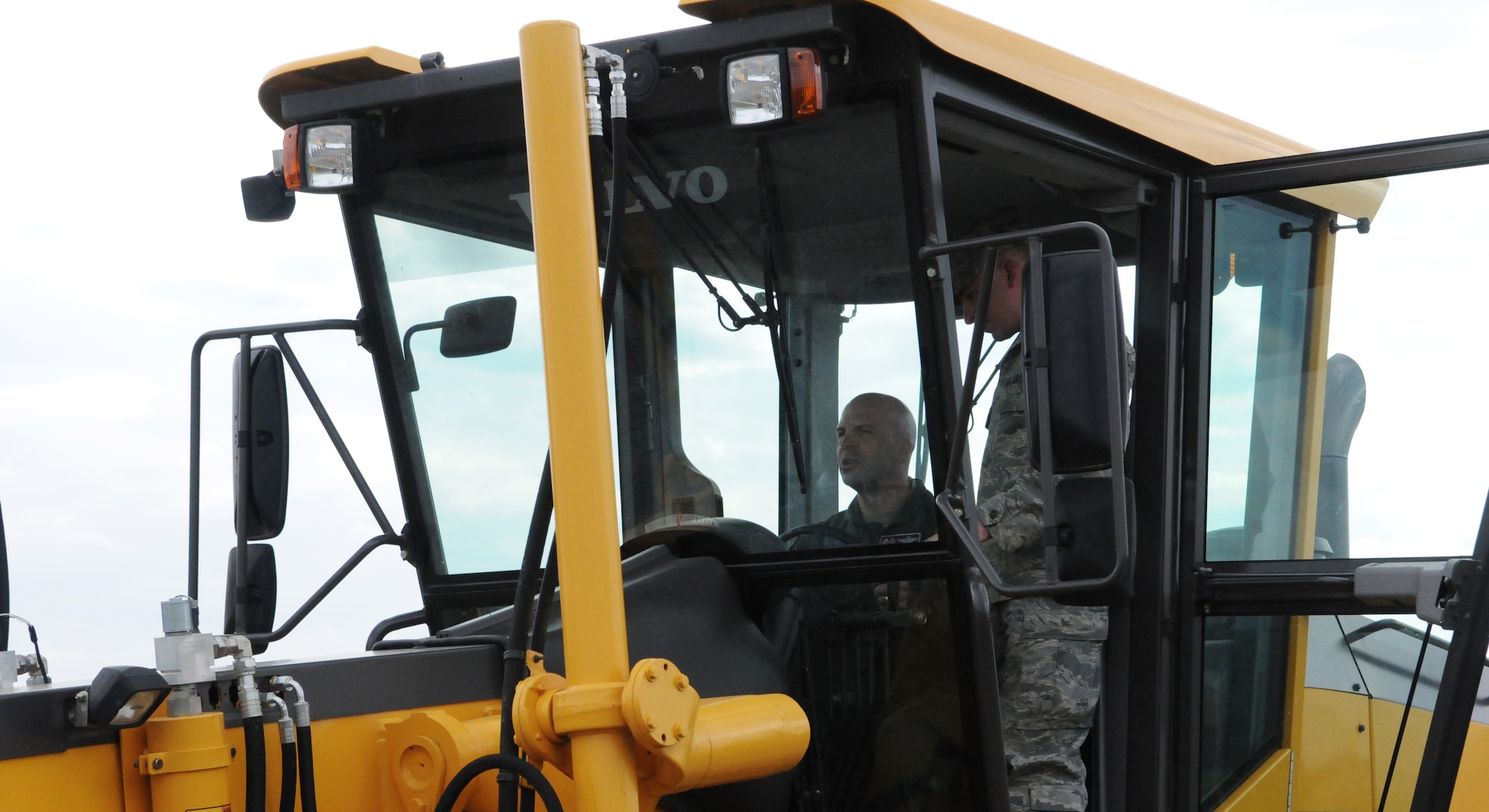 RAF MILDENHALL, England -- Col. Chad Manske, 100th Air Refueling Wing commander (seated), receives instruction from Senior Airman Billy Crocker, 100th Civil Engineer Squadron, on how to operate a road grater at the fire department's live-fire training area Aug. 11. Visiting workcenters across the base allows base leadership to see the work their Airmen perform on a daily basis. (U.S. Air Force photo/Staff Sgt. Thomas Trower) 