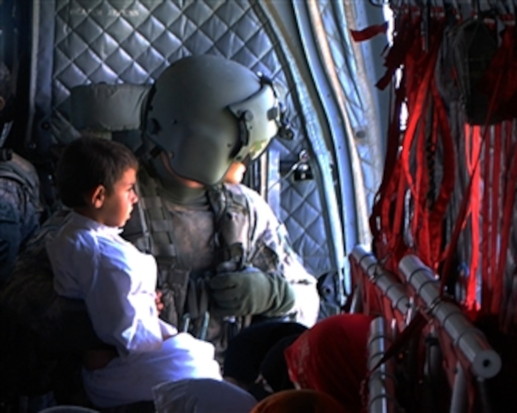 U.S. Army Sgt. Kristopher Perkins (right) a CH-47 Chinook helicopter crew chief with Bravo Company, Task Force Raptor, 3rd Combat Aviation Brigade holds a child in his lap after picking up 114 Pakistani flood victims during flood relief missions out of the Swat valley in Pakistan on Aug. 11, 2010.  