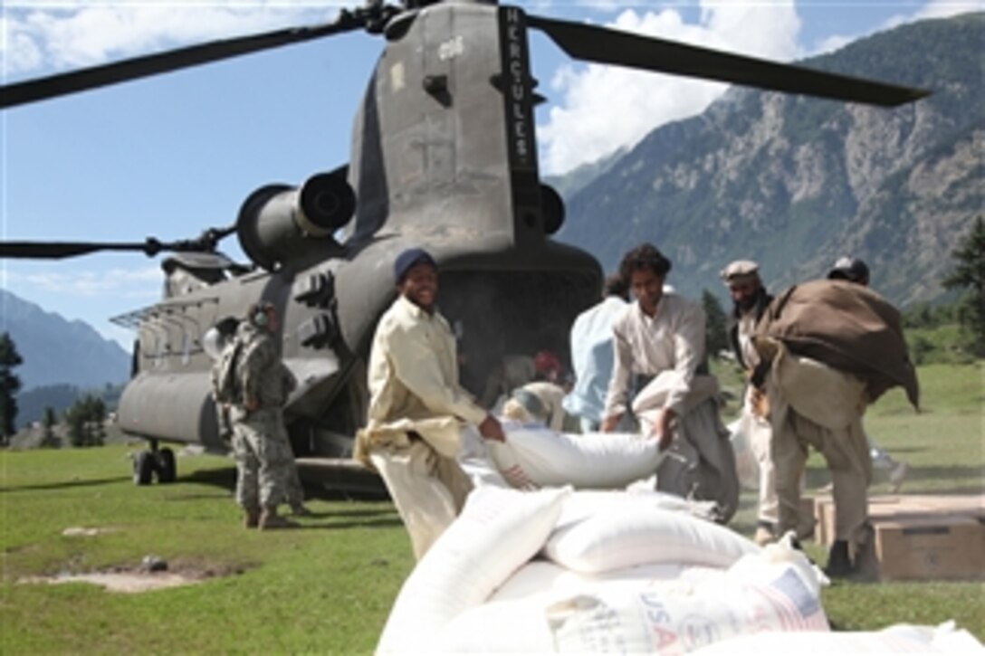 Pakistani men throw a bag of flour onto a pile behind a U.S. Army CH-47 Chinook helicopter that arrived to deliver humanitarian assistance and help with the evacuation of flood victims in the Swat Valley of Pakistan during the flood disaster recovery effort in Khyber Pakhtunkhwa province on Aug. 11, 2010.  
