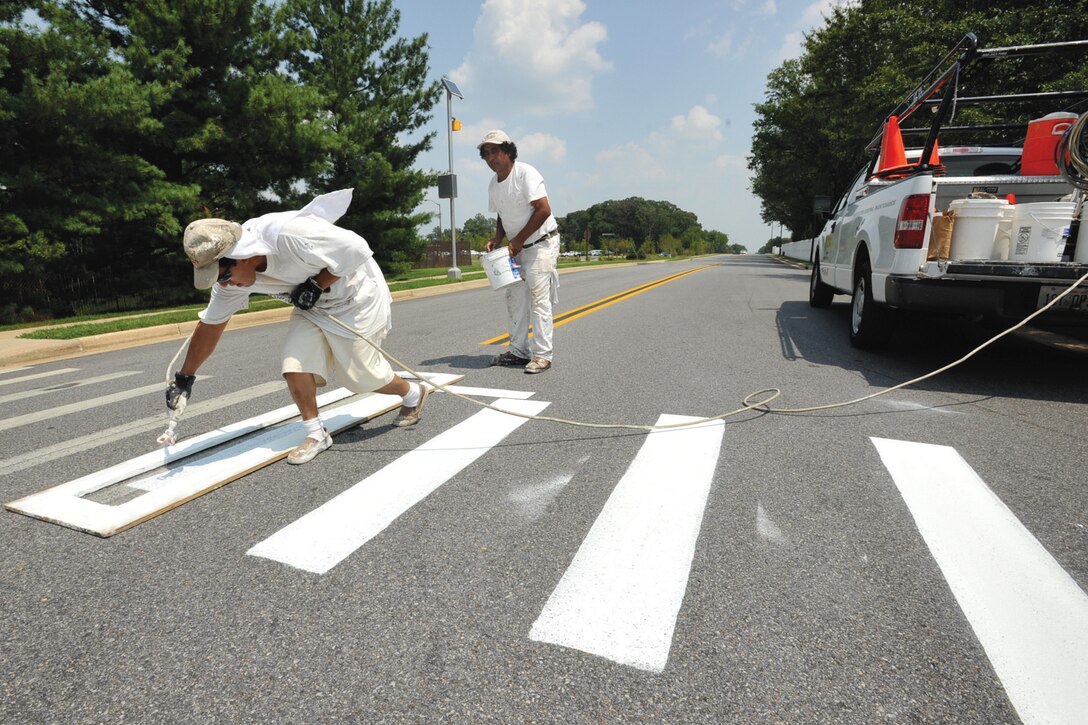 Contract painters, Rene Veizaga, left, paints road crossing lines, and his co-worker,  Fernardo Esabar, prepares to apply sealant to paint at the intersection of Tuskeegee and Menoher Drive as part of the base beautification project Monday. The entire base is slotted to receive the roadway facelift.