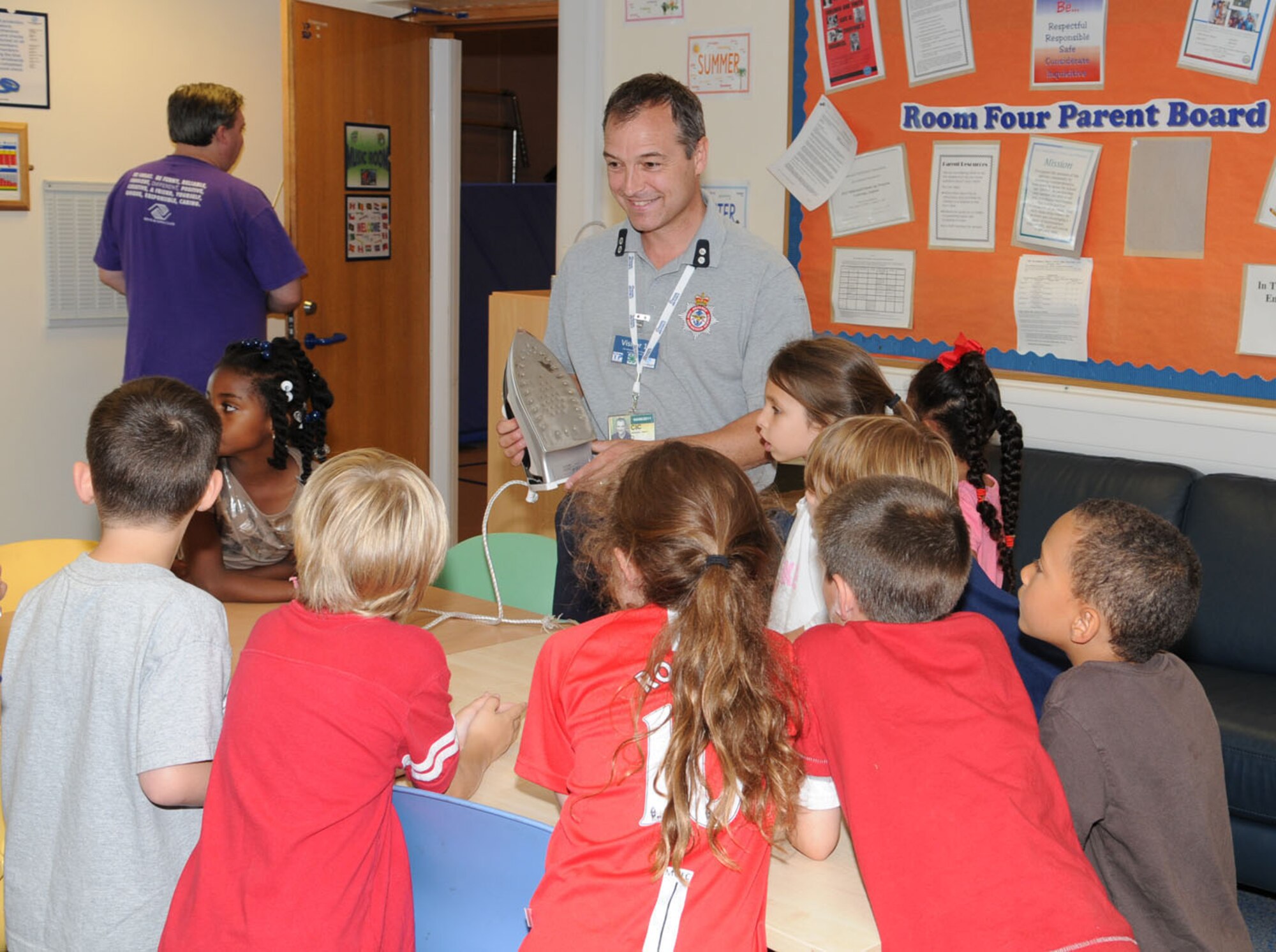 RAF MILDENHALL, Engalnd -- Firefighter Adrian Delaney, 100th Civil Engineer Fire Department fire prevention office, talks with children from Room 23 (6- to 8-year-olds) about different fire safety hazards. The fire department put on a special fire prevention event for the children in summer camp at the youth center Aug. 9. They had a fire safety room (shown here), large inflatable slide, metal sled, and a fire muster, where children wore a firefighter's helmet and held different objects, while going around a small course. Sparky the Fire Dog also visited the children during the event. (U.S. Air Force photo/Karen Abeyasekere)