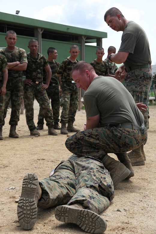 Gunnery Sgt. Miles S. Beasley, native of Spokane, Wash., and platoon sergeant of Company A, 2nd Assault Amphibian Battalion, Ground Combat Element of Special-Purpose Marine Air-Ground Task Force Continuing Promise 2010, instructs Colombian Marines on proper takedown techniques during non-lethal weapons training at Colombian Marine Corps Training Base Covenas in Colombia, Aug. 14, 2010. (Standing) Staff Sgt. Gabriel Delarosa, native of Holland, Mich., and section leader, translates English to Spanish to ensure Colombian Marines understand how to execute the technique. Marines from USS Iwo Jima conducted subject matter expert exchanges with Colombian Marines Aug. 9-17 in support of Operation Continuing Promise 2010.