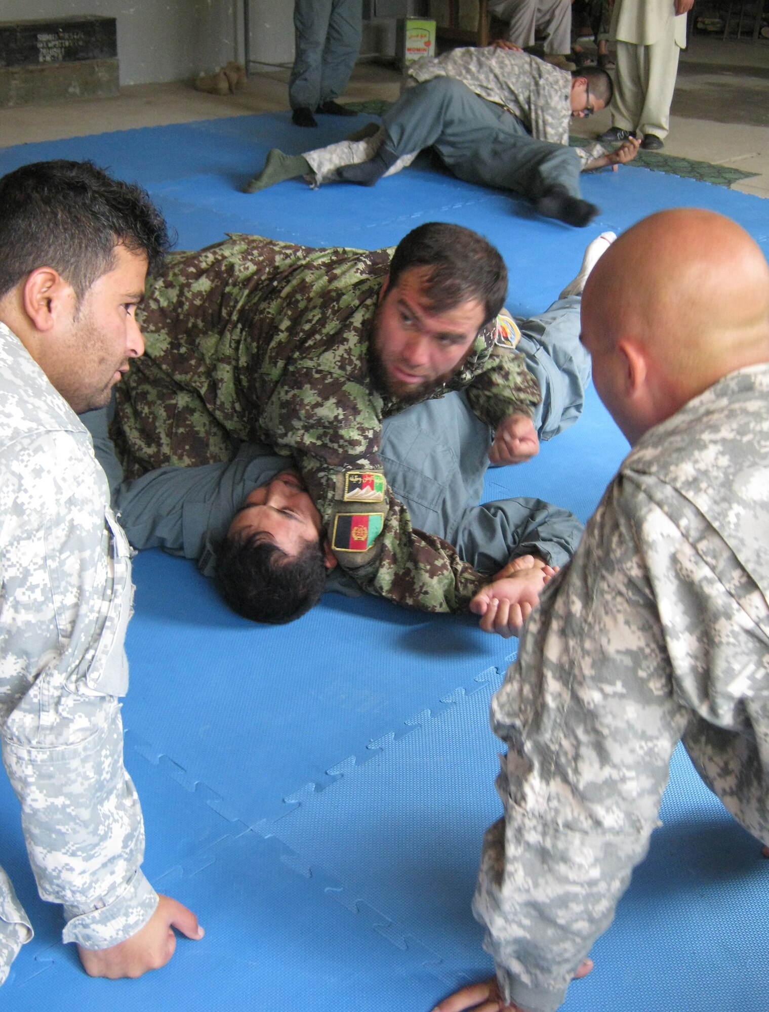 Afghan National Army Maj. Azizullah Aziz, Panjshir Operations Coordination Center-Provincial, holds down Afghan National Police Capt. Safat Ullah Sangee, OCC-P, while U.S. Army Staff Sgt. Daniel Cornell (right), a Philadelphia native and member of the Task Force Wolverine Embedded Training Team with Provincial Reconstruction Team Panjshir, instructs Aziz through an interpreter. ANP trainers began learning U.S. Army Combatives techniques Aug. 14 so they can teach the skill to other ANP officers in each of the seven districts in the Panjshir Province, Afghanistan. (Photo by U.S. Air Force 2nd Lt. Jason Smith, PRT Panjshir Public Affairs)