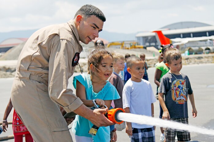 Lance Cpl. Jeremy Borges, a station Aircraft Rescue and Firefighting specialist, assists Allison Mohn, a 5-year-old School Age Care child, shoot a water hose at cones during an airfield facilities tour here Aug. 17. SAC children from around the station spent two days learning what the Marines do here.