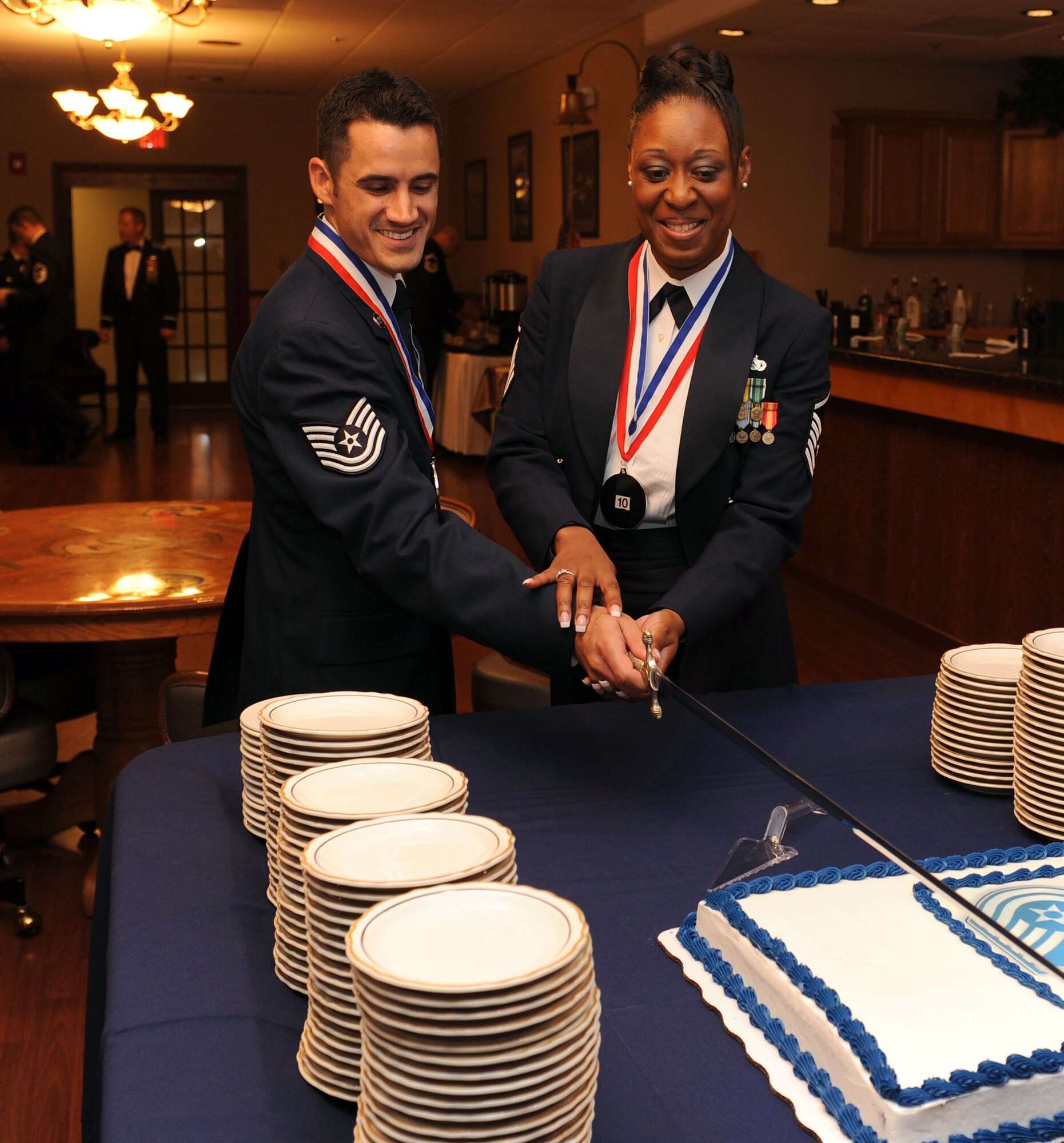 Master Sgt. Natasha Thomas, a 314th Aircraft Maintenance Squadron inductee, and Tech. Sgt. Parker Alford, a 19th Logistics Readiness inductee, prepare to cut the cake at the Senior NCO Induction Ceremony Aug. 13 at Hangar 1080. Sergeant Thomas was the senior ranking inductee present and Sergeant Alford had the highest line number of the inductees. (U.S. Air Force photo by Senior Airman Steele C. G. Britton)