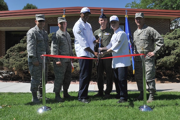 Col. Stephen N. Whiting, 21st Space Wing commander (center) is flanked by Airman 1st Class Derek Woolbright-Hutchins (left) and Airman 1st Class Brandon Gillespie, both dining hall staffers, to cut the ribbon for the official grand reopening of the Aragon dining facility Aug. 6. The dining hall had been closed since April while it was renovated with a new heating, ventilating and air conditioning unit, new restroom facilities, a handicap accessible doorway and a new, modern motif. (U.S. Air Force photo/Rob Bussard)