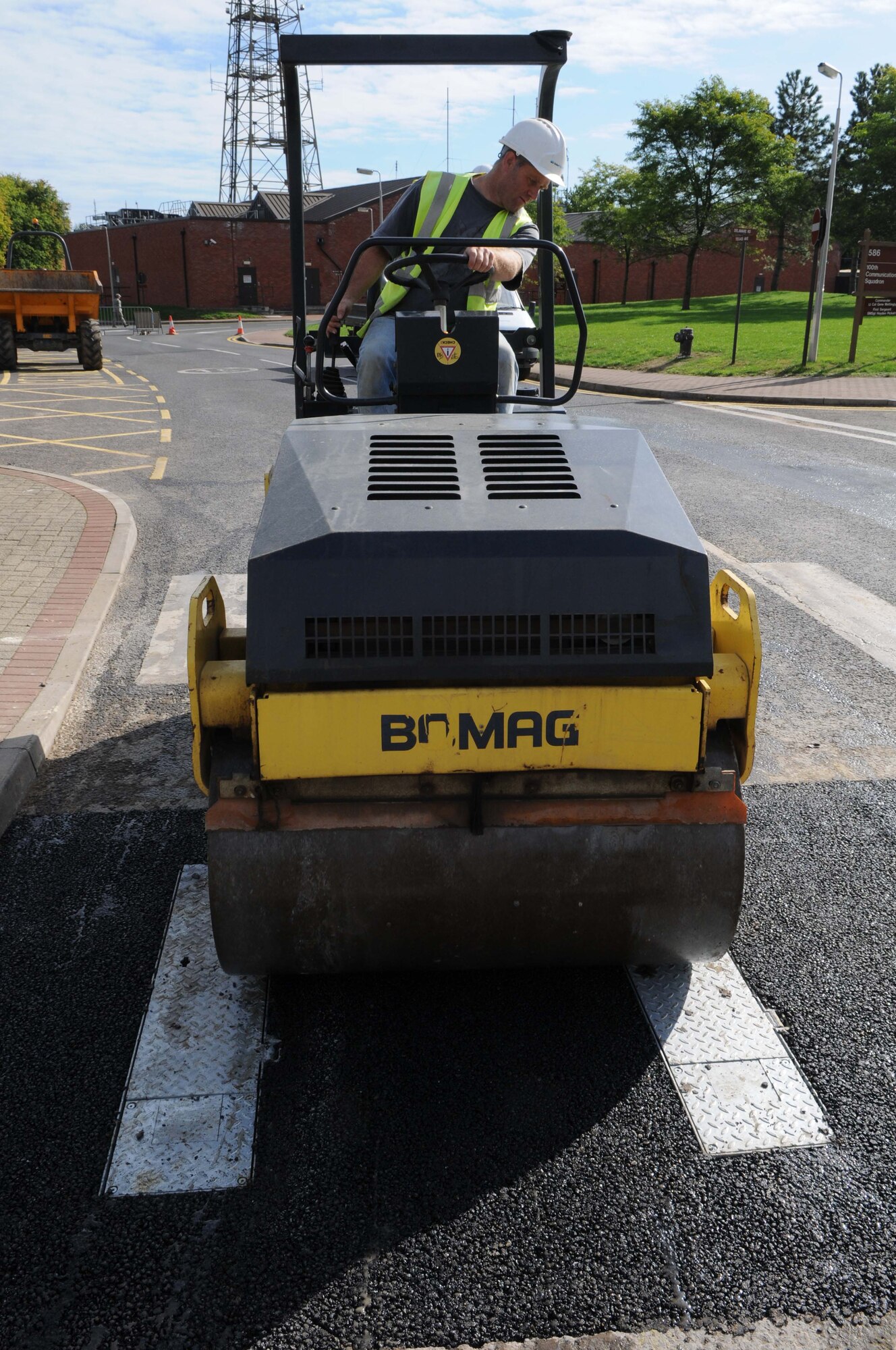 RAF MILDENHALL, England -- Paul Wiseman, a local contractor, compacts freshly laid asphalt around newly installed bollards using a Bomag 120 roller Aug. 18 here. These bollards increase safety and security around high population areas. (U.S. Air Force photo/Senior Airman Ethan Morgan)