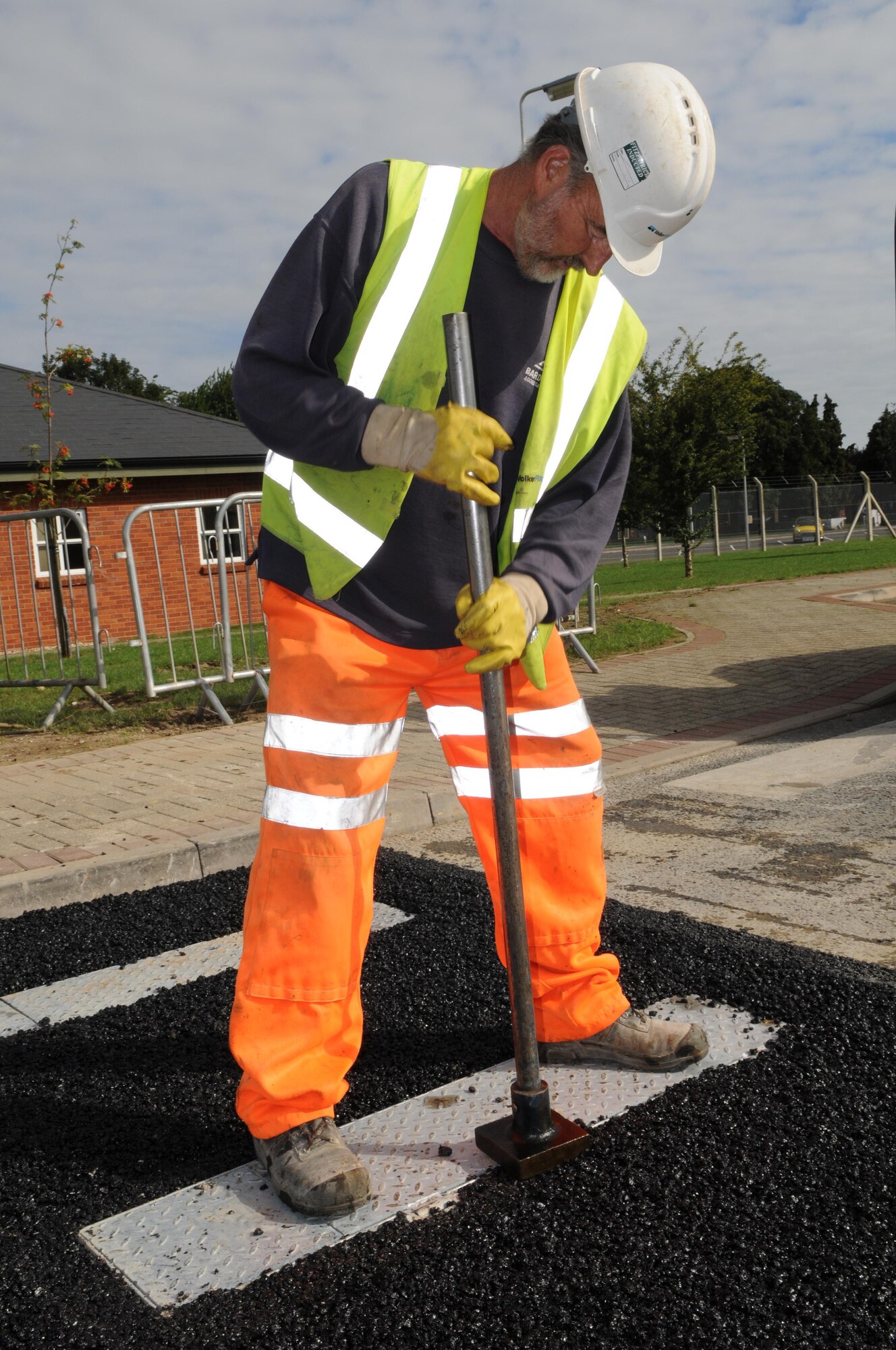 RAF MILDENHALL, England -- Marlrn King, a local contractor, uses a pounder to compact freshly laid asphalt around newly installed bollards Aug. 18 here. The pounder is used to compact asphalt that the larger Bomag 120 roller can't reach. (U.S. Air Force photo/Senior Airman Ethan Morgan)