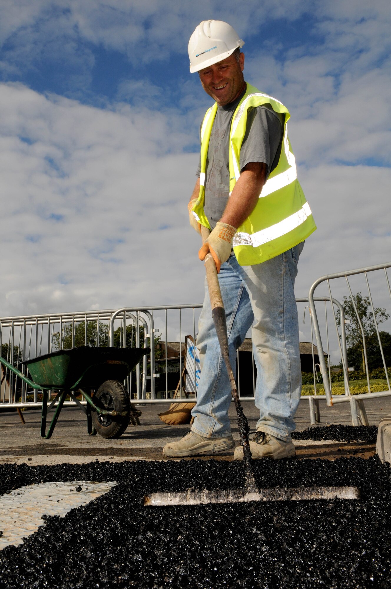 RAF MILDENHALL, England -- Paul Wiseman, a local contractor, uses a rake to smooth freshly laid asphalt around newly installed bollards Aug. 18 here. The bollards are being installed around the base including areas deemed to have high population density. (U.S. Air Force photo/Senior Airman Ethan Morgan)
