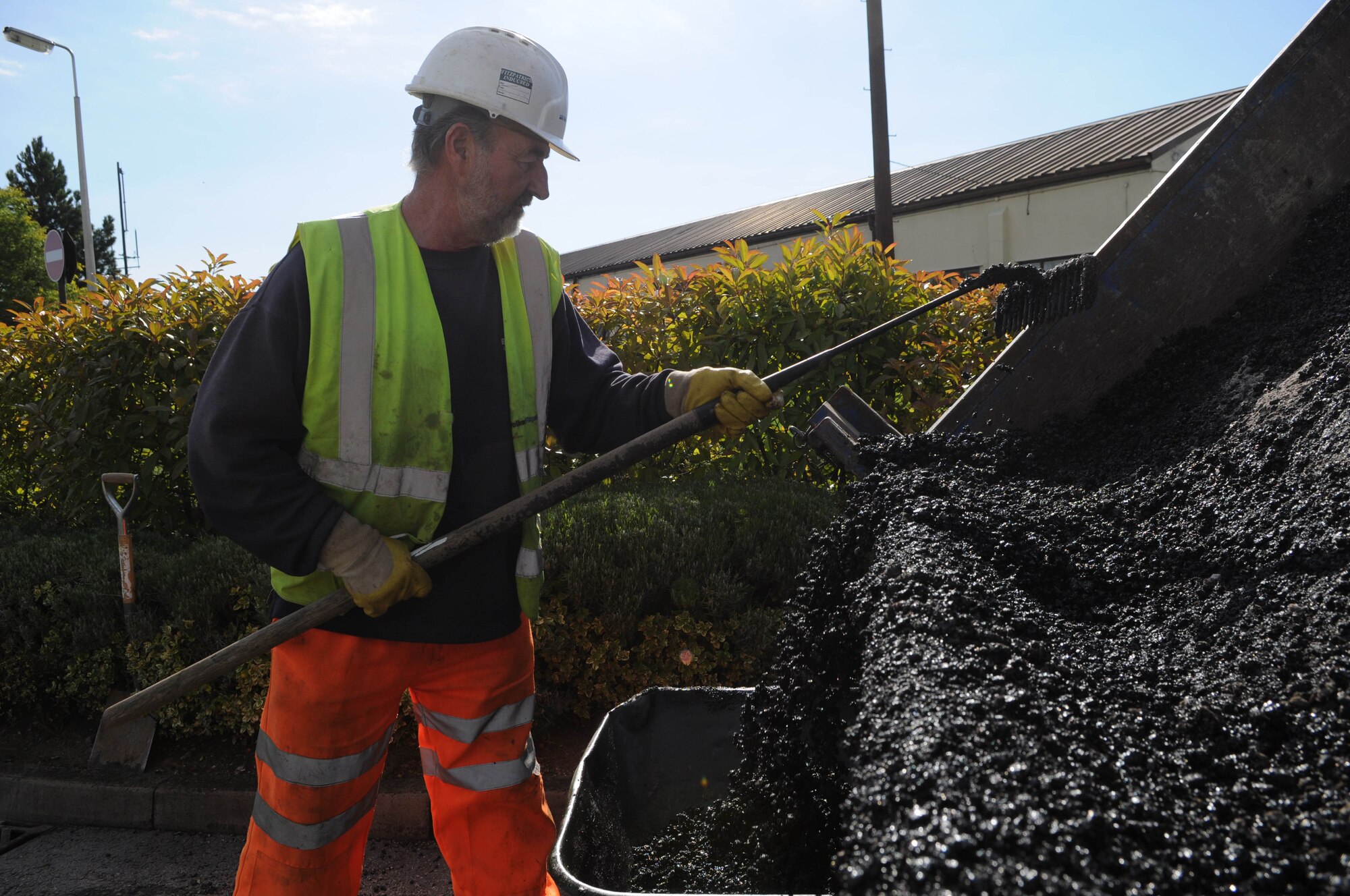 RAF MILDENHALL, England -- Marlrn King, a local contractor, rakes out fresh asphalt into a wheelbarrow to ready it for transport Aug. 18 here. This along with other construction projects around the base are being implemented to improve the base's safety and security. (U.S. Air Force photo/Senior Airman Ethan Morgan)