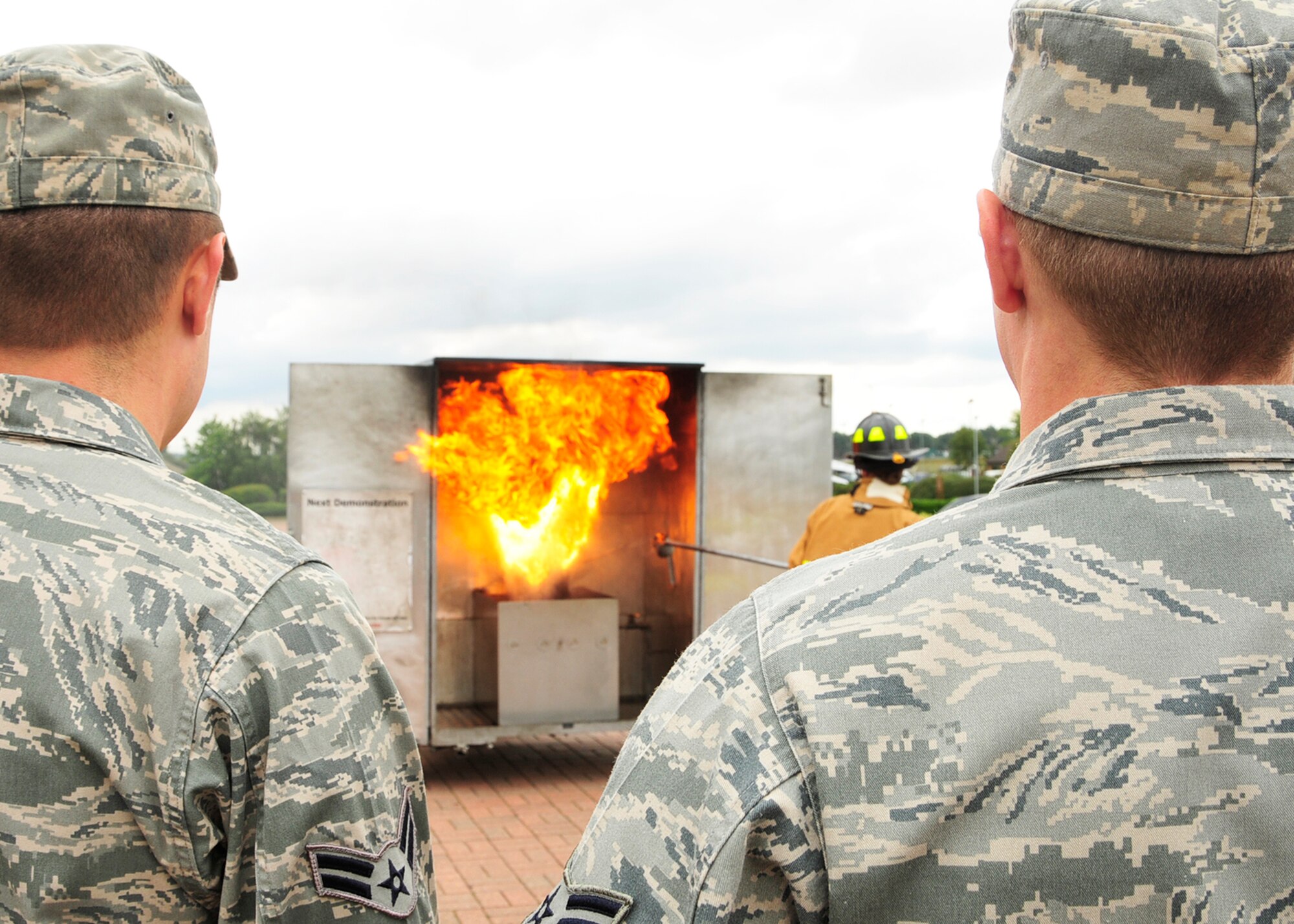Airmen 1st Class Michael Melancon, (left), and Andrew Blakeman, (right), 48th Civil Engineer Squadron engineering apprentices, stop to watch Tech. Sgt. Carrie Frederickson, (center), 48th Civil Engineer Squadron fire inspector, demonstrate how not to put out a grease fire by pouring a cup of water onto the flaming pot during a fire safety demonstration outside the RAF Lakenheath base commissary Aug. 13.  Tech. Sgt. Nathan Elkins, 48th Civil Engineer Squadron fire inspector, provided information and tips on fire safety as Sergeant Frederickson demonstrated how to properly and improperly extinguish a grease fire. (U.S. Air Force photo/Airman 1st Class Tiffany Deuel)