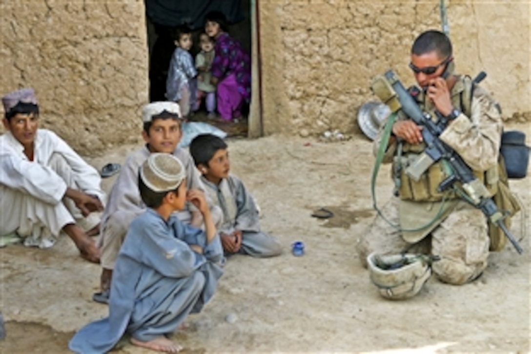 U.S. Marine Corps Lance Cpl. Jack Hamilton calls in his position to headquarters while taking a rest to play with Afghan children during a census operation in Marja, Afghanistan, Aug. 16, 2010. The squad came under attack halfway through the patrol and engaged enemy Taliban in the process. Hamilton is a rifleman with Golf Company, 2nd Battalion, 9th Marine Regiment.