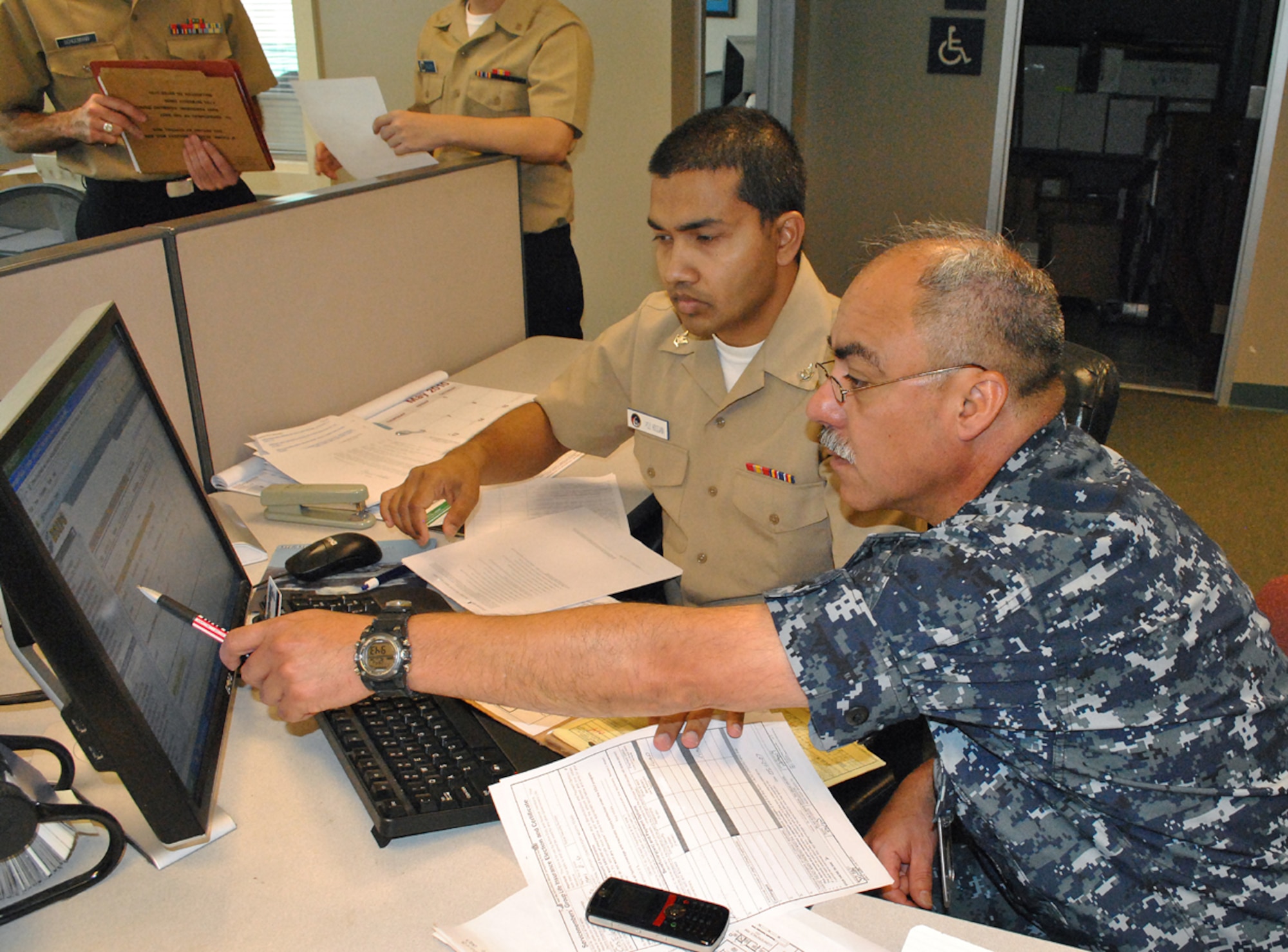 Chief Hospital Corpsman Hugo A. Castellanos, right, a Reserve Component member assigned to Operational Health Support Unit, Dallas, Detachment F, works with Personnel Specialist 3rd Class Mukarram Hossain, manpower clerk at Navy Operational Support Center Fort Worth, as they review Castellano's Electronic Service Record data in the Navy Standard Integrated Personnel System. Image edited for security purposes. (U.S. Navy photo/Senior Chief Mass Communication Specialist Maria R. Escamilla)