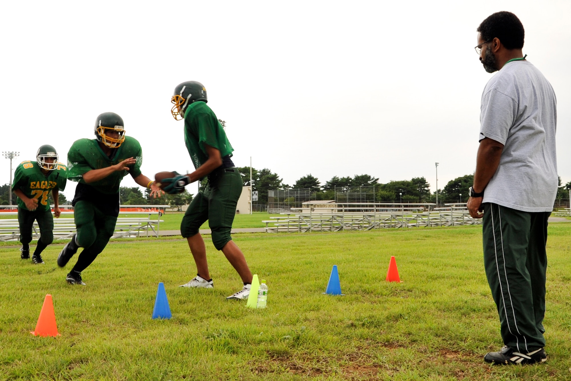 MISAWA AIR BASE, Japan -- Edgren Eagles high school football players gear up for their upcoming season. Coach Butch Austin watches quarterback Louis Murphy hand off the ball to fullback Aric Butterfield, with tailback James Bowman (left) following Butterfield through the hole during an offensive play. The Eagles have 50 players; 24 returning from last year with eight of them being seniors. Eagles coaching staff consist of eight coaches. (U.S. Air Force photo/Tech. Sgt. Russell McBride)