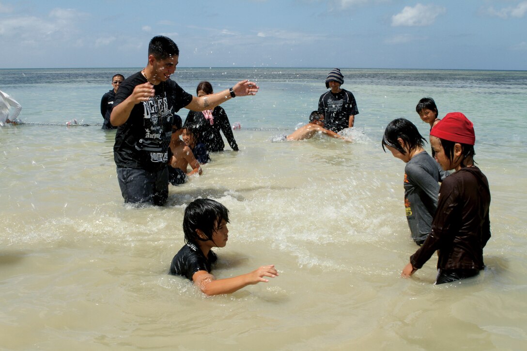 Lance Cpl. Anthony Garcia, a motor transport mechanic with Maintenance Company, 3rd Maintenance Battalion, Combat Logistics Regiment 35, 3rd Marine Logistics Group, III Marine Expeditionary Force, plays in the ocean with children from Tai Chu En Orphanage Aug. 21. Approximately 35 Marines and sailors gathered at Torii Beach to spend the afternoon with the children for an annual beach bash.