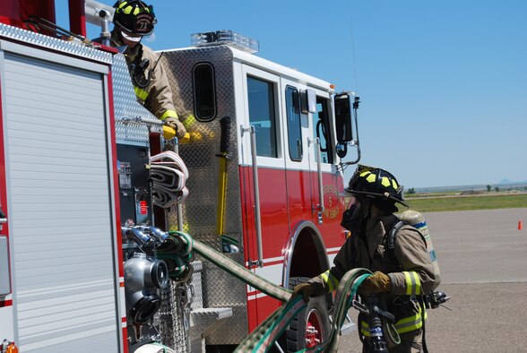 Airman 1st Class Nathan Johnson, 341st Civil Engineering Squadron firefighter, deploys a hand line from a fire engine during training at the base fire department July 8. Airman 1st Class Mark Martin, 341st CES firefighter, assists from inside the vehicle. (U.S. Air Force photo/Airman 1st Class Kristina Overton)