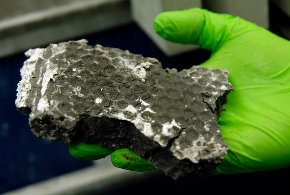 IWTP operator Nick Flynt holds a dried piece of industrial sludge that is scraped from a plate and frame filter press after 3,500 pounds per square inch of pressure has dewatered and dried it. Removal costs of the waste are lowered as all water is removed. The waste water goes through other processes at the Tinker plant to clean it.