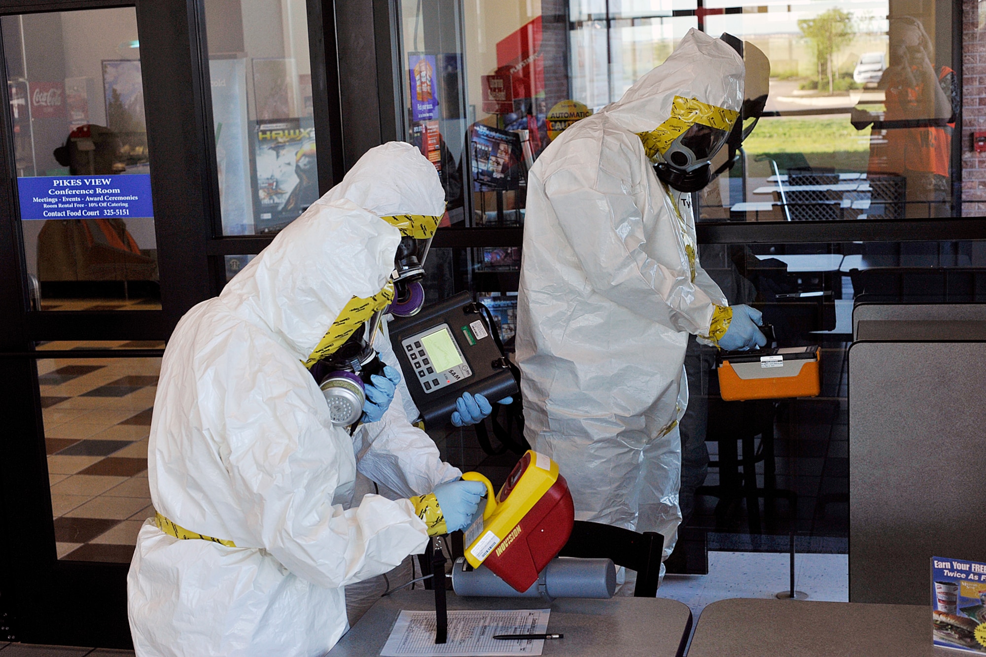 Members of Peterson’s bioenvironmental engineering team investigate a possible radiological agent planted at the Peterson Base Exchange food court, where seven base members who had exhibited signs of radioactive poisoning had eaten in the days prior. The investigation and emergency response was part of the quarterly Condor Crest exercise on Peterson Air Force Base Aug. 16 to 20. The scenario allowed responders to practice response to a radiological event. (U.S. Air Force photo/Larry Hulst)