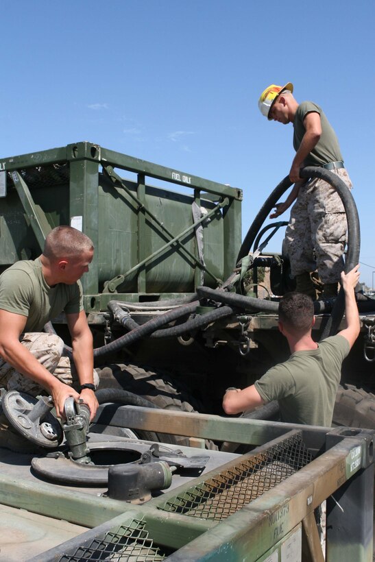 Pfc. Gregory M. Tessmer, a bulk fuel specialist with Marine Wing Support Squadron 373, feeds a hose to Lance Cpl. Travis Potter and Lance Cpl. Michael Magaris, also bulk fuel specialists with MWSS-373, to add fuel to a 600-gallon reserve tank Aug. 25. The tanks are used to supply fuel to aircraft and ground vehicles.