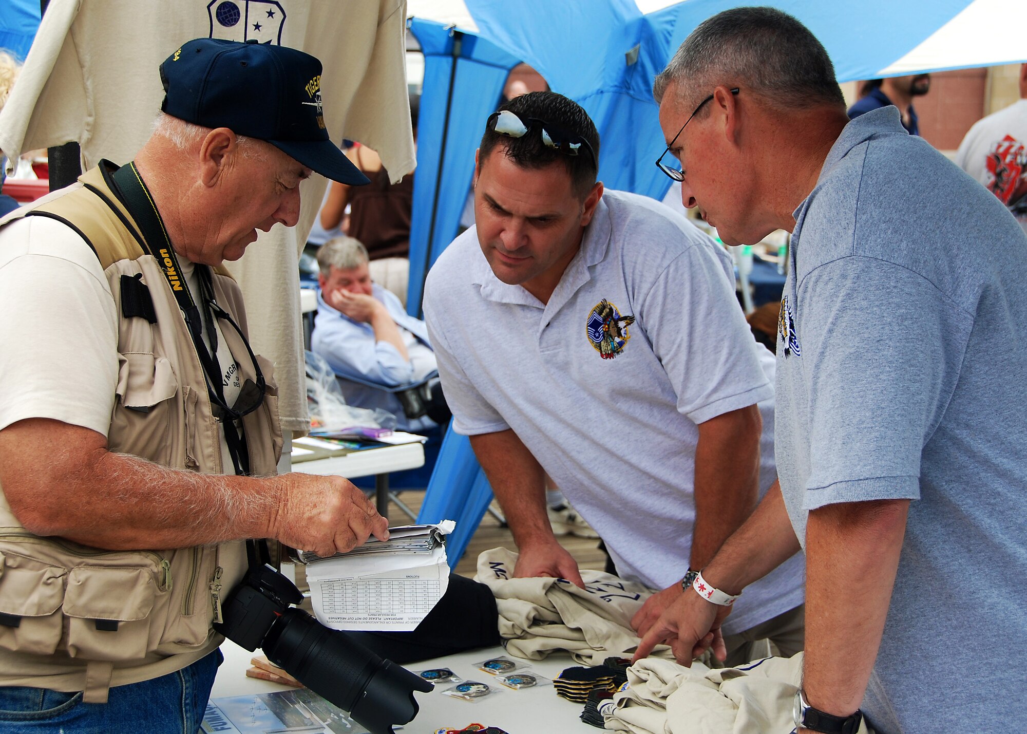 ATLANTIC CITY, N.J. ? Chief Master Sgt. James Whiteley (right) and Chief Master Sgt. Todd Harris (center) look at a customer?s photos while working at a souvenir booth during an air show in Atlantic City, N.J., Aug. 25, 2010. Proceeds from the souvenirs are used to fund Airmen academic scholarships, purchase holiday gift baskets and provide other need-based assistance to Airmen of the 514th Air Mobility Wing. Chief Whiteley is a member of the 514th Maintenance Squadron, and Chief Harris is a member of the 714th Aircraft Maintenance Squadron.