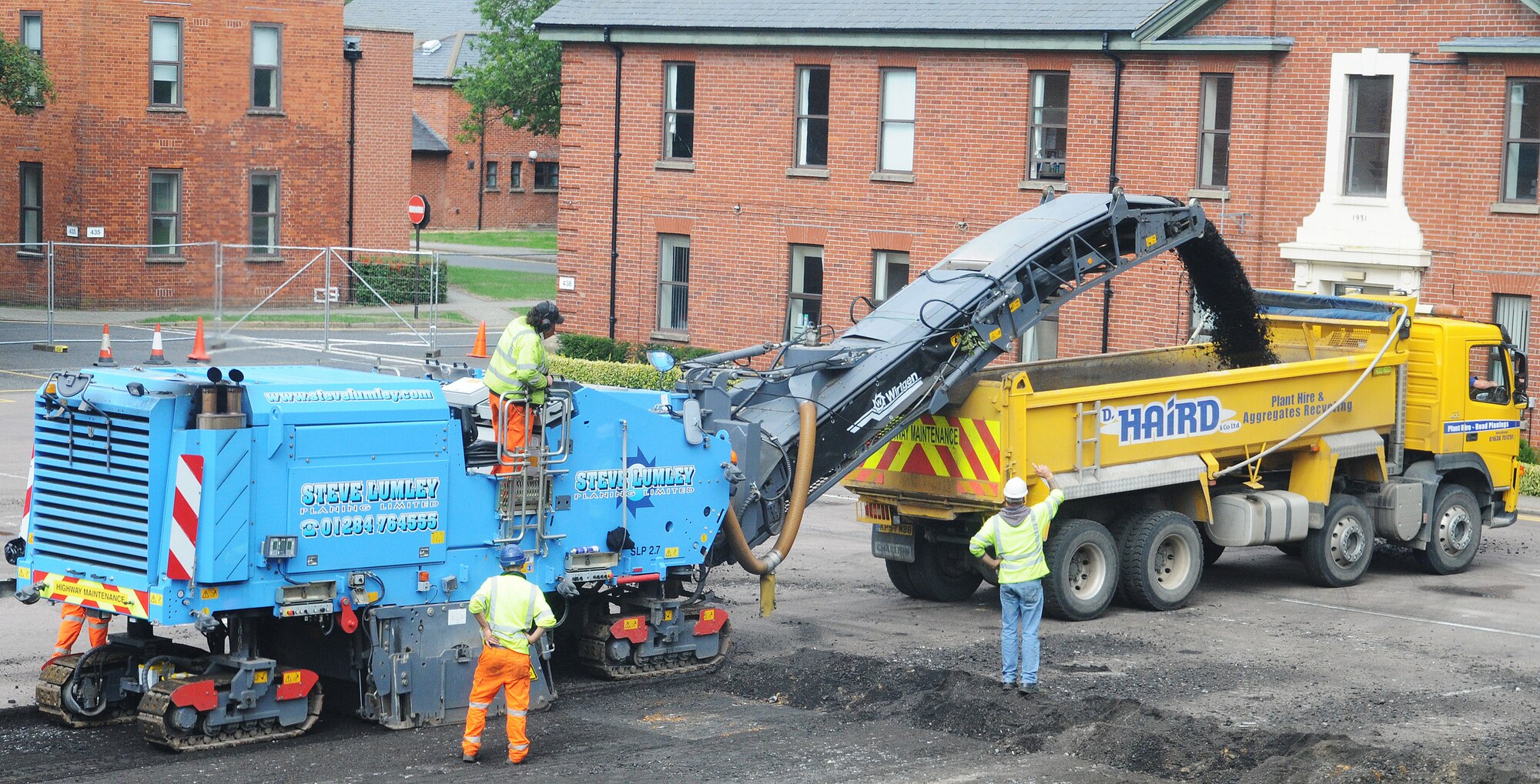 RAF MILDENHALL, England -- Local contractors use a road planer to remove about 170 millimeters of concrete with into the back of a dump truck in the initial stages of construction at Washington Square here. About 1,600 tons of concrete were removed from the square in a few days to begin transforming the parking lot into a pedestrian-friendly green space. (U.S. Air Force photo/Staff Sgt. Thomas Trower)