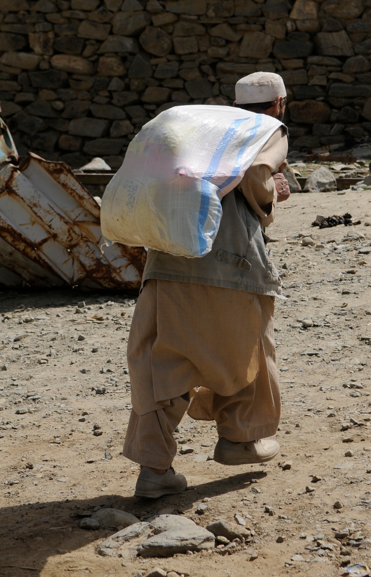 An elder carries a sack of food provided to his family after their village was damaged by a flood in early August.  With the help of the Dara Afghan National Police, the executive district manager of the Abdullah Khel Valley in the Dara District, led the distribution of humanitarian aid consisting of food and cooking items to those affected by the flooding. The local government identified families requiring aid, developed a plan of distribution and executed that plan with minimal Provincial Reconstruction Team  Panjshir oversight. (U.S. Air Force photo by: Tech. Sgt. Sean Mateo White, PRT Panjshir photographer)