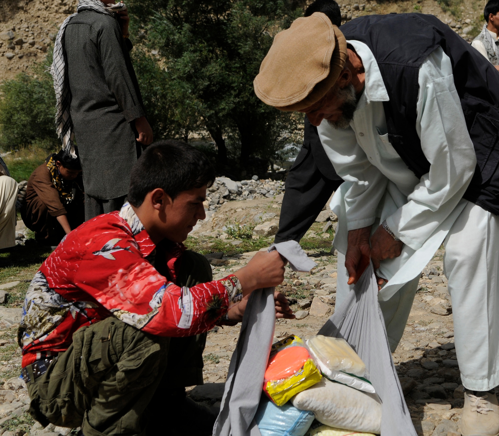 A young man assists his father by carrying food provided to his family after their village was damaged by a flood in early August.  With the help of the Dara Afghan National Police, the executive district manager of the Abdullah Khel Valley in the Dara District, led the distribution of humanitarian aid consisting of food and cooking items to those affected by the flooding. The local government identified families requiring aid, developed a plan of distribution and executed that plan with minimal Provincial Reconstruction Team  Panjshir oversight. (U.S. Air Force photo by: Tech. Sgt. Sean Mateo White, PRT Panjshir photographer)