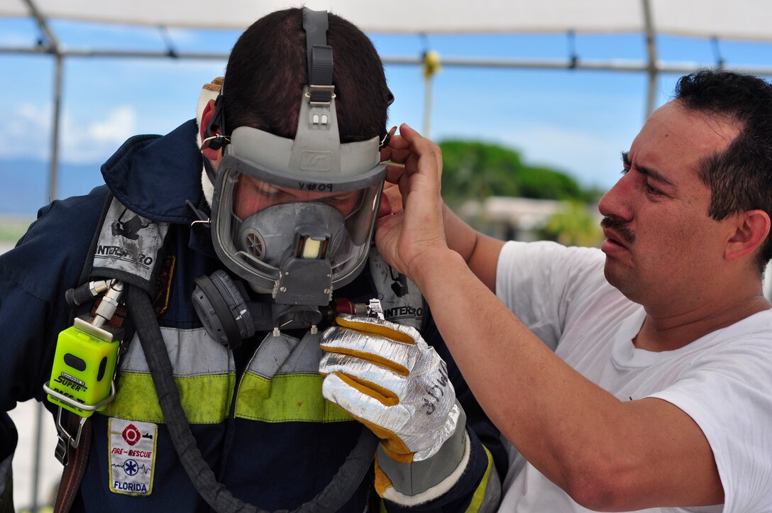 SOTO CANO AIR BASE, Honduras --  Jose Alberto Portillo, left, a firefighter from Tegucigalpa, Honduras, gets assistance from Henry Noj, a Guatemalan firefighter, in putting on his personal protective equipment during the Central America Sharing Mutual Operational Knowledge and Experiences exericse here Aug. 24. This year's firefighter training exercise included firefighters from Honduras, the 612th Air Base Squadron and, for the first time, Guetamala. (U.S. Air Force photo/Martin Chahin)